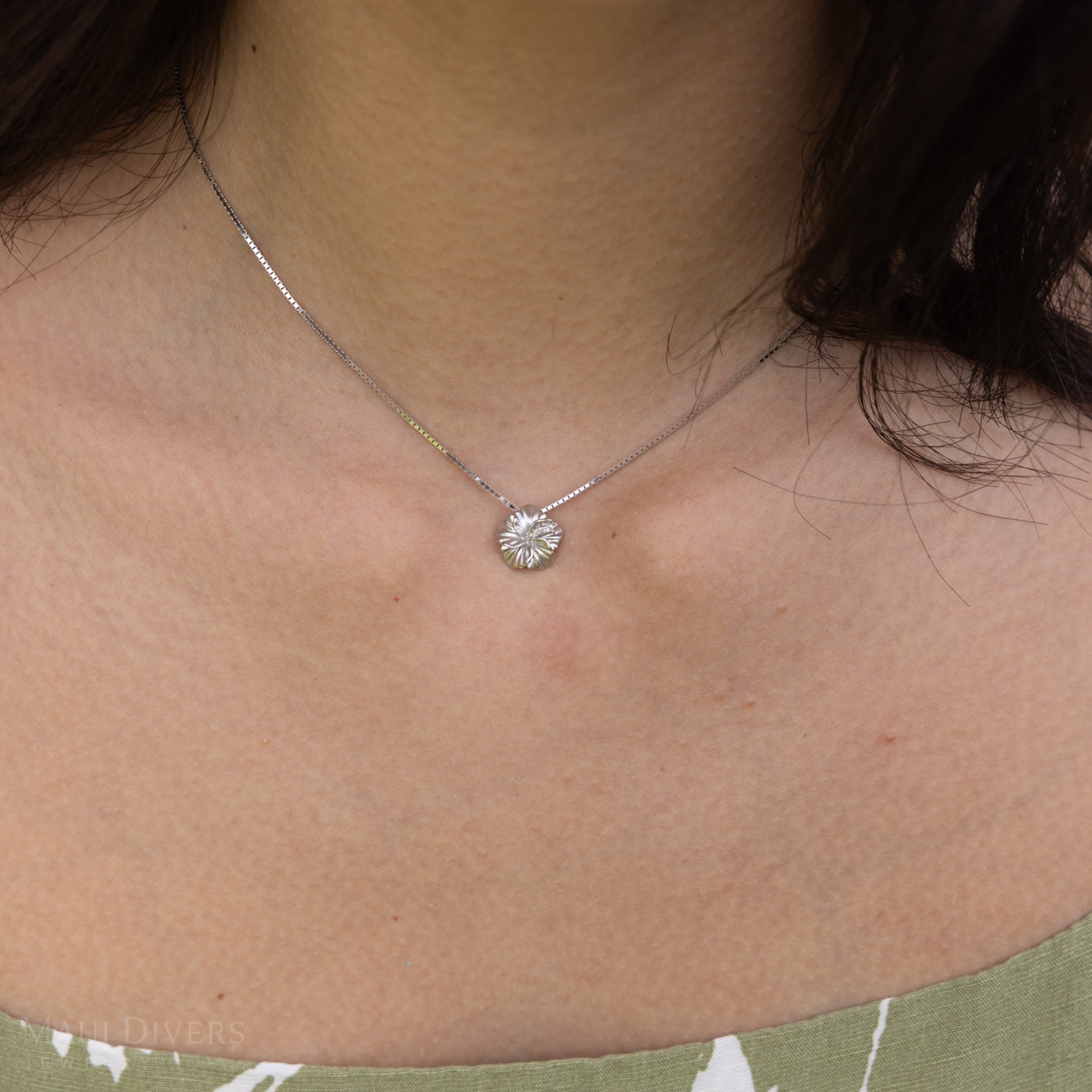 Close up of a woman wearing a white gold hibiscus pendant on a box chain