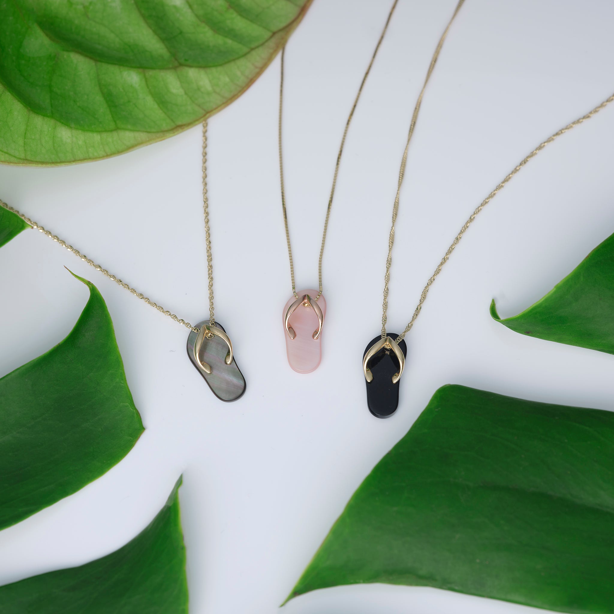 Black Coral, Black Mother of Pearl and Pink Coral Slippers Pendant in Gold next to leaves