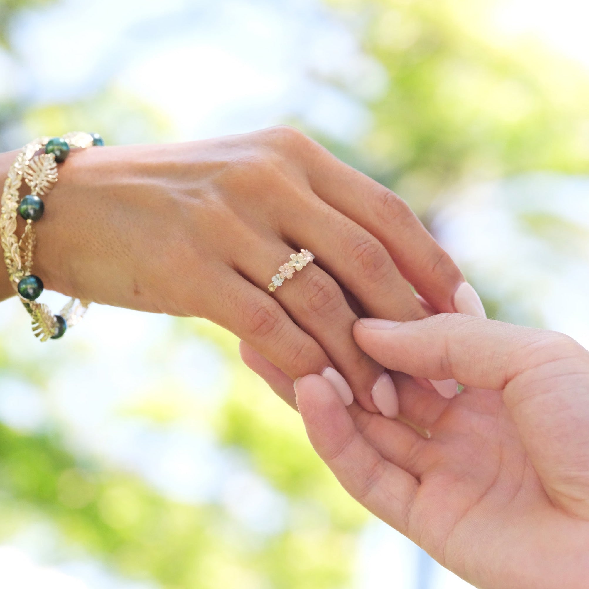 A woman's hand with a Plumeria Ring in Tri Color Gold with Diamonds holding another hand