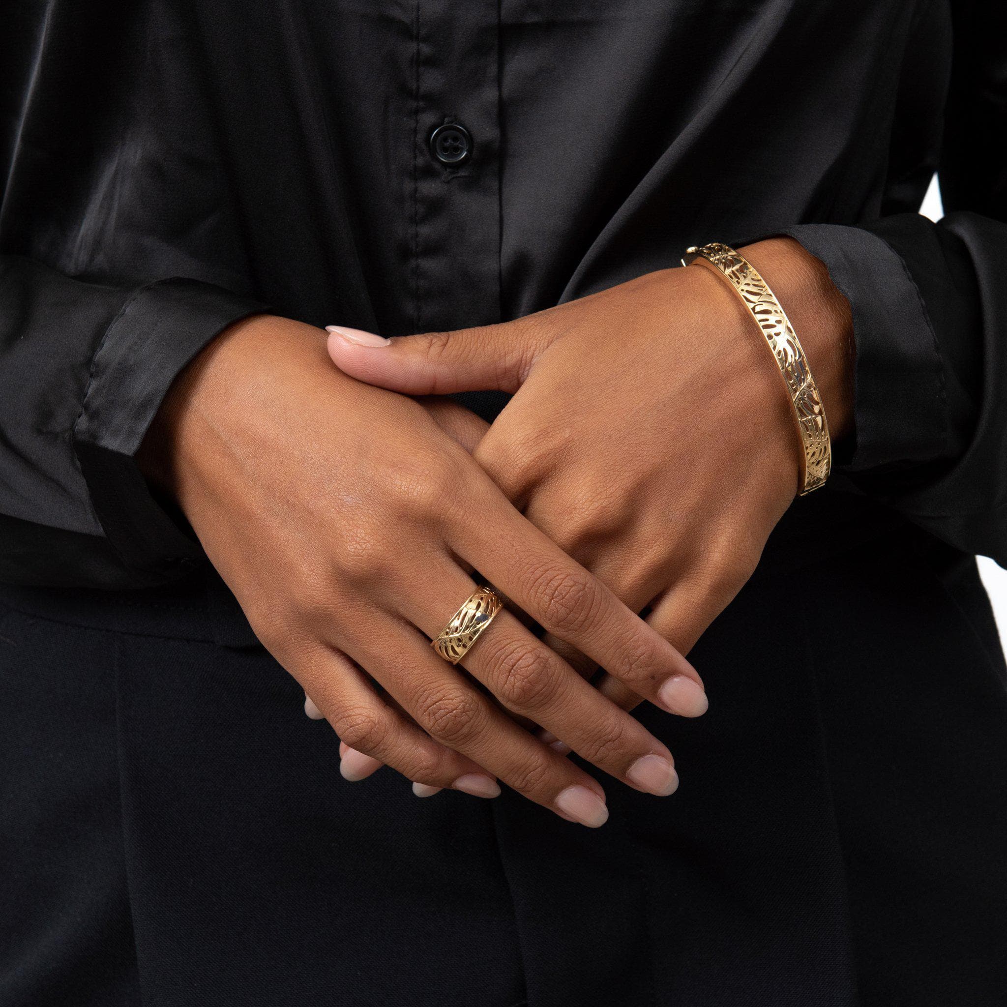 A woman's hand wearing a Monstera Ring and Bracelet in Gold against black clothing