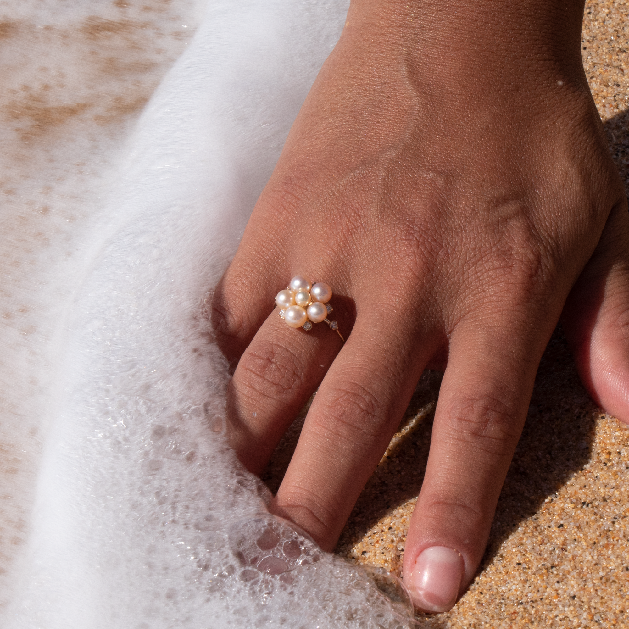 A woman's hand in the sand wearing a Tiny Bubbles Peach Freshwater Pearl Ring in Gold with Diamonds - Maui Divers Jewelry