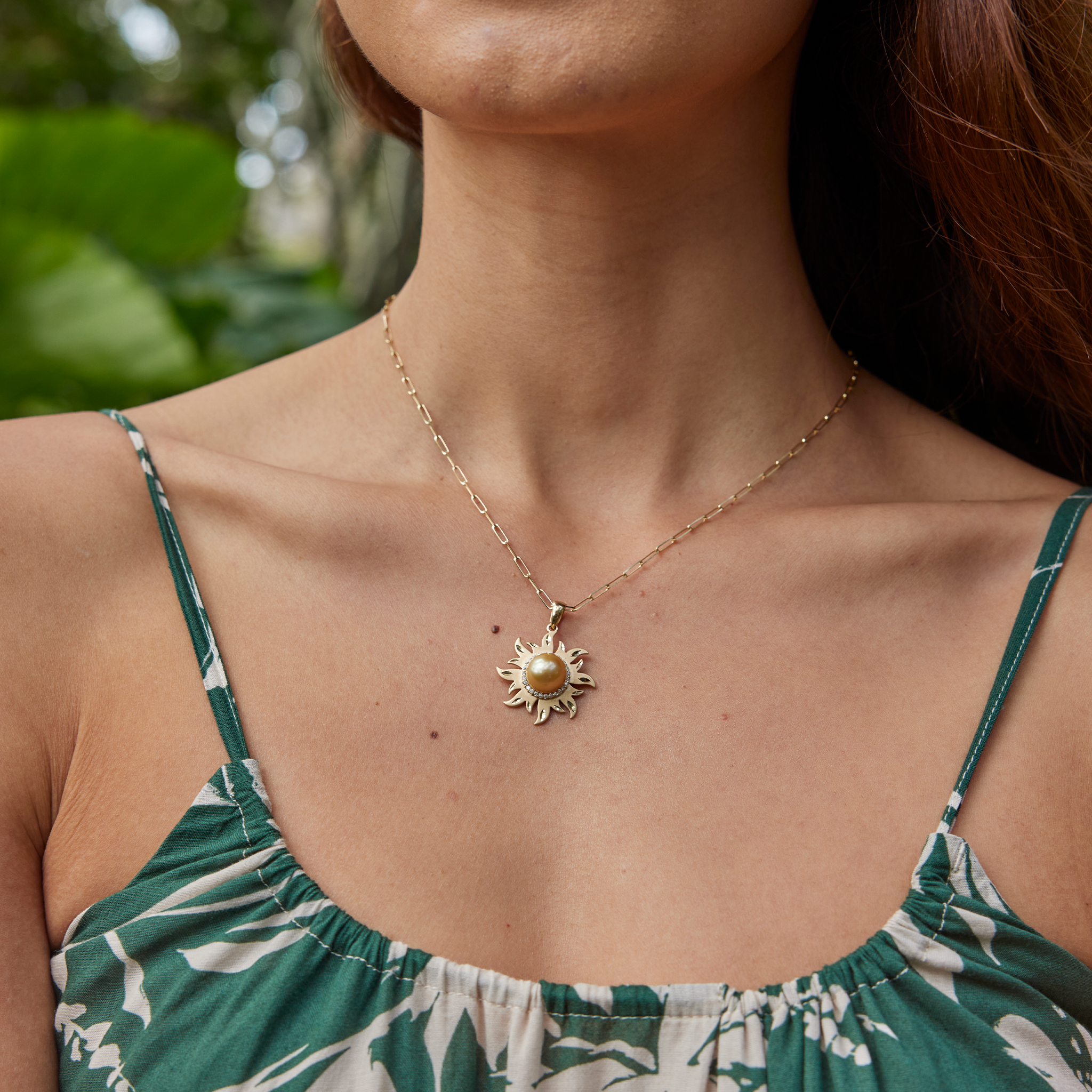 Diamond South Sea gold pearl sun pendant in 14k yellow gold on a paperclip chain, worn by a woman in a green patterned top.