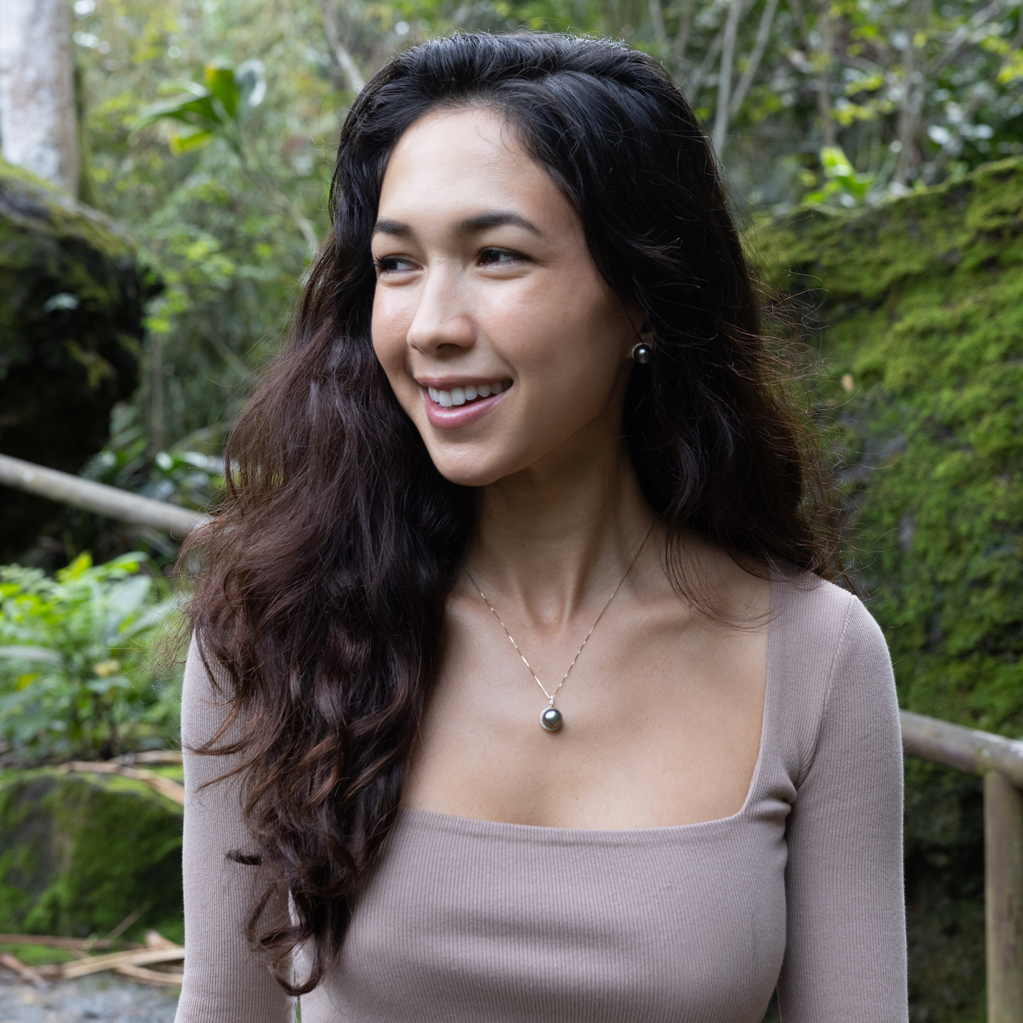 Woman wearing a diamond halo Tahitian black pearl pendant and earrings with a mossy forest background