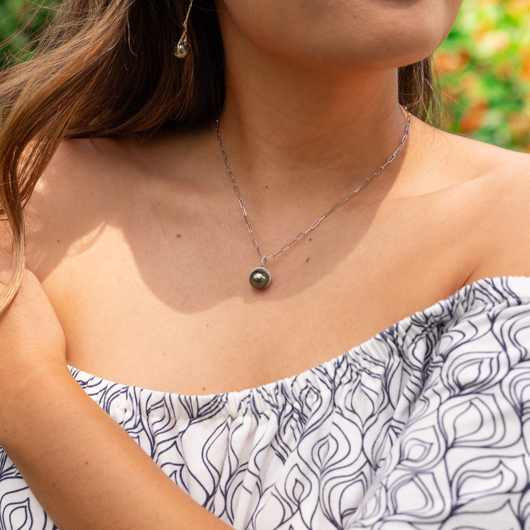Woman wearing a diamond halo Tahitian black pearl pendant on a white gold paperclip chain