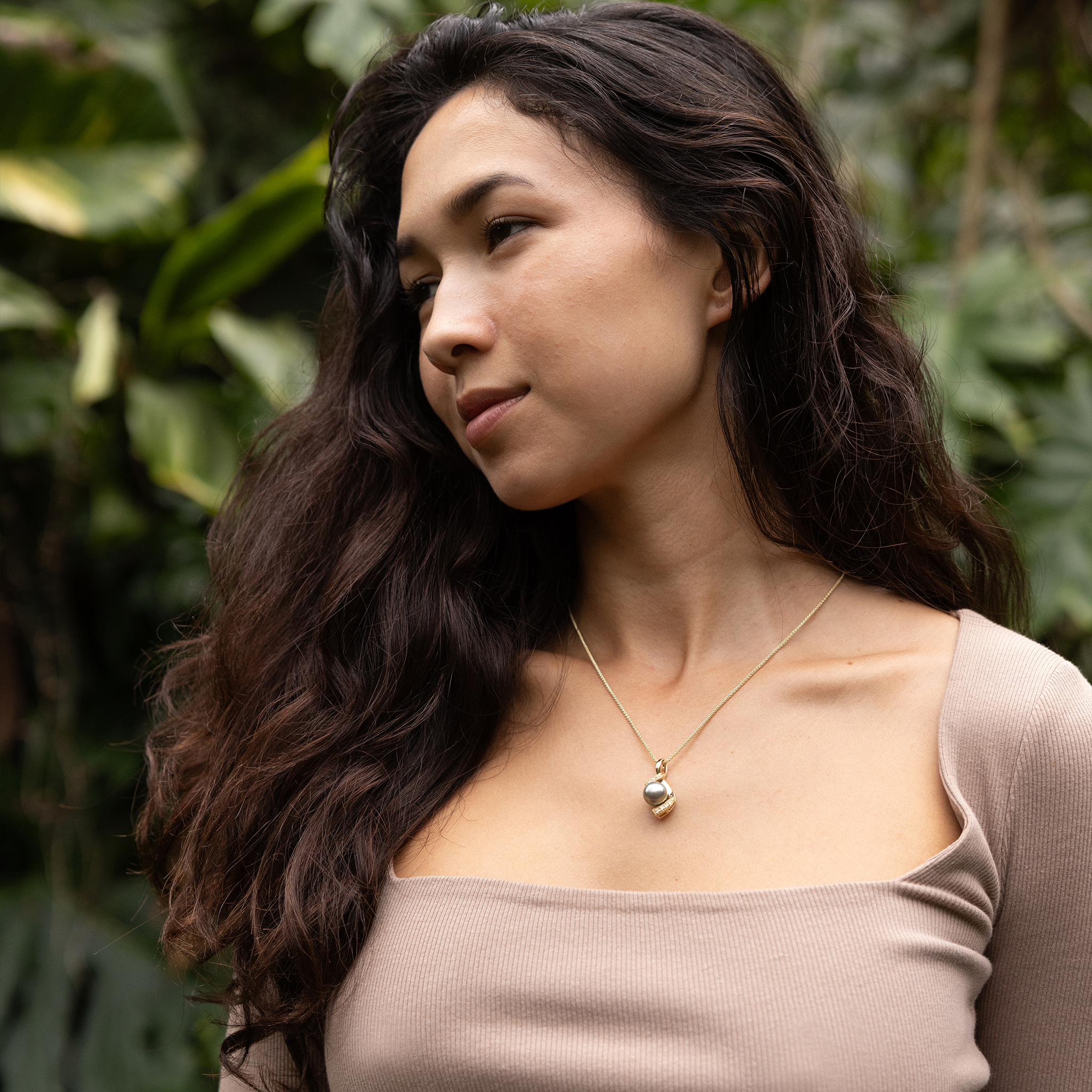 Woman wearing a diamond, Tahitian black pearl necklace with a blurred leafy background