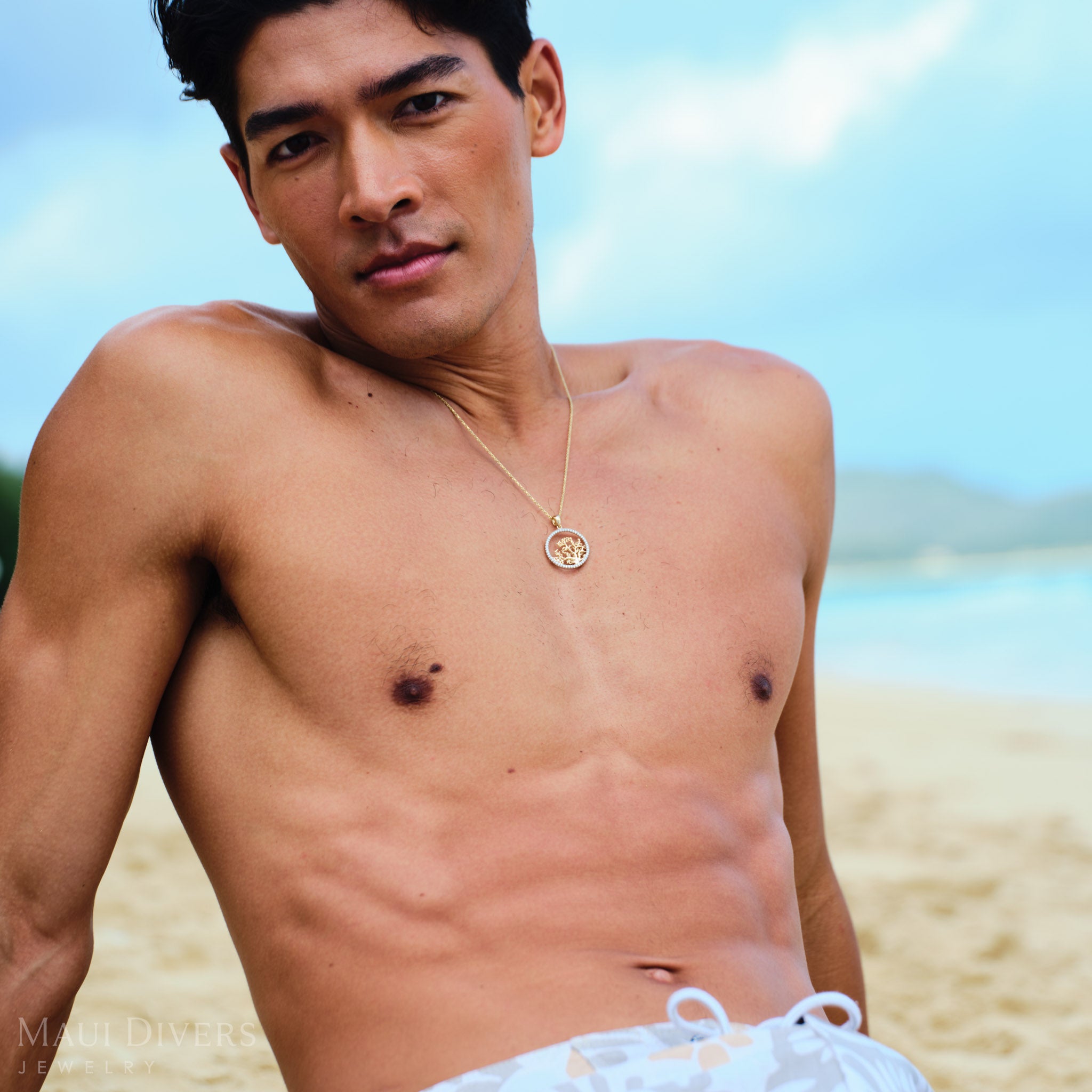 Man leaning back on a beach wearing a gold coral branch pendant with diamonds