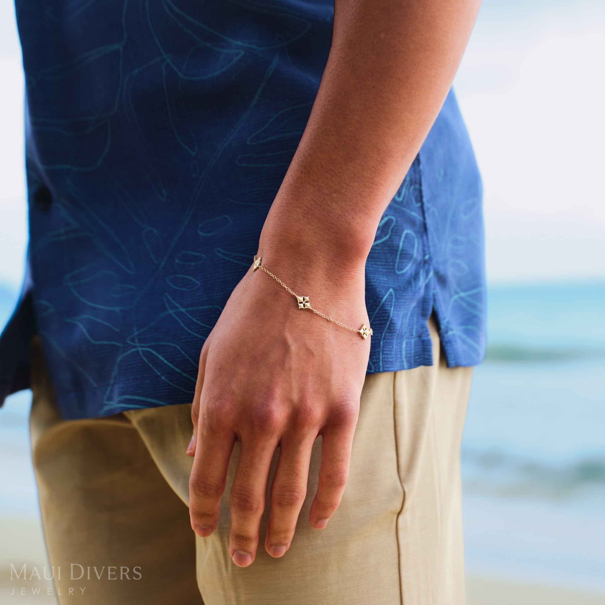 Person wearing a gold Hawaiian quilted star bracelet on a blurred beach background