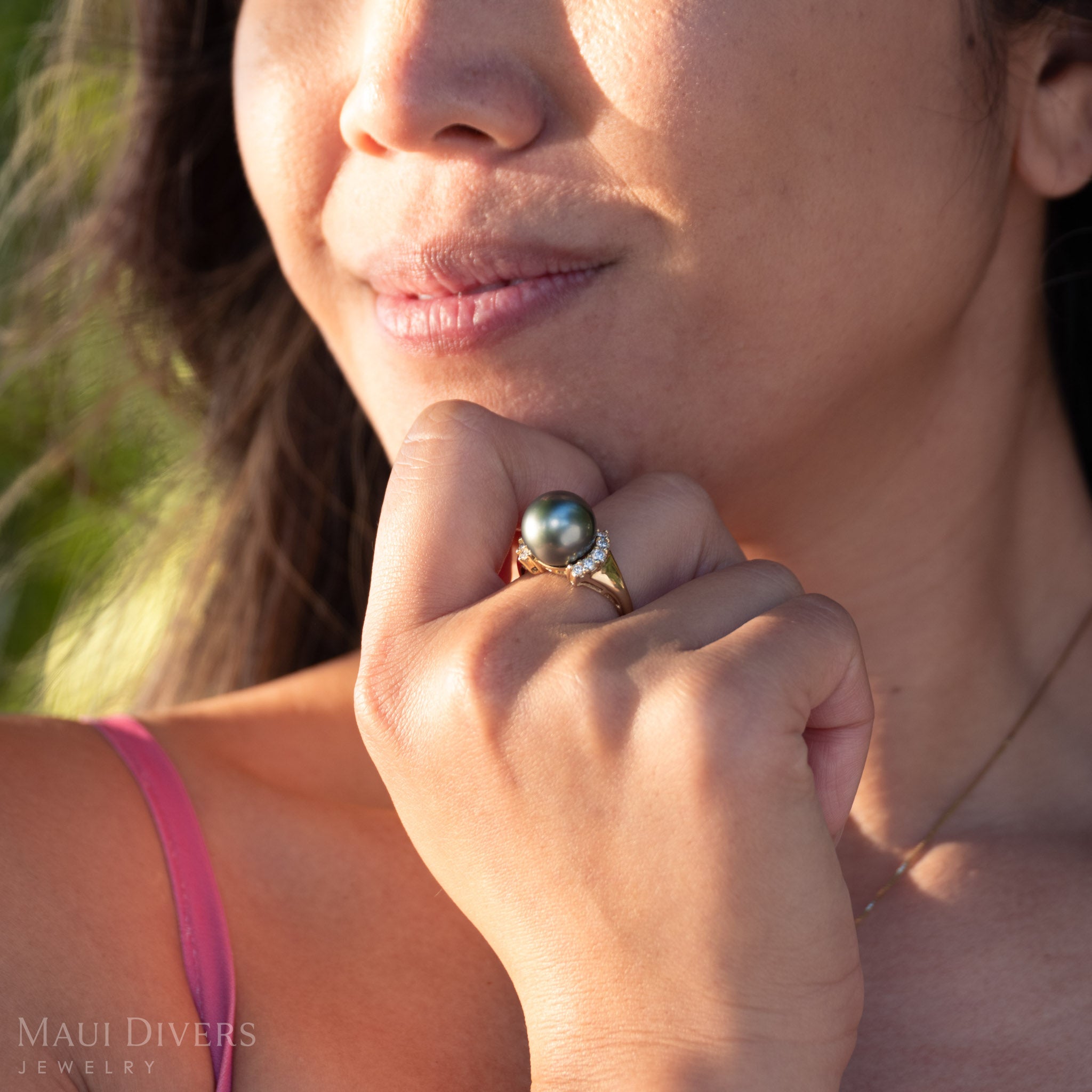 Close-up of a person wearing a ring with a large Tahitian black pearl, outdoors.
