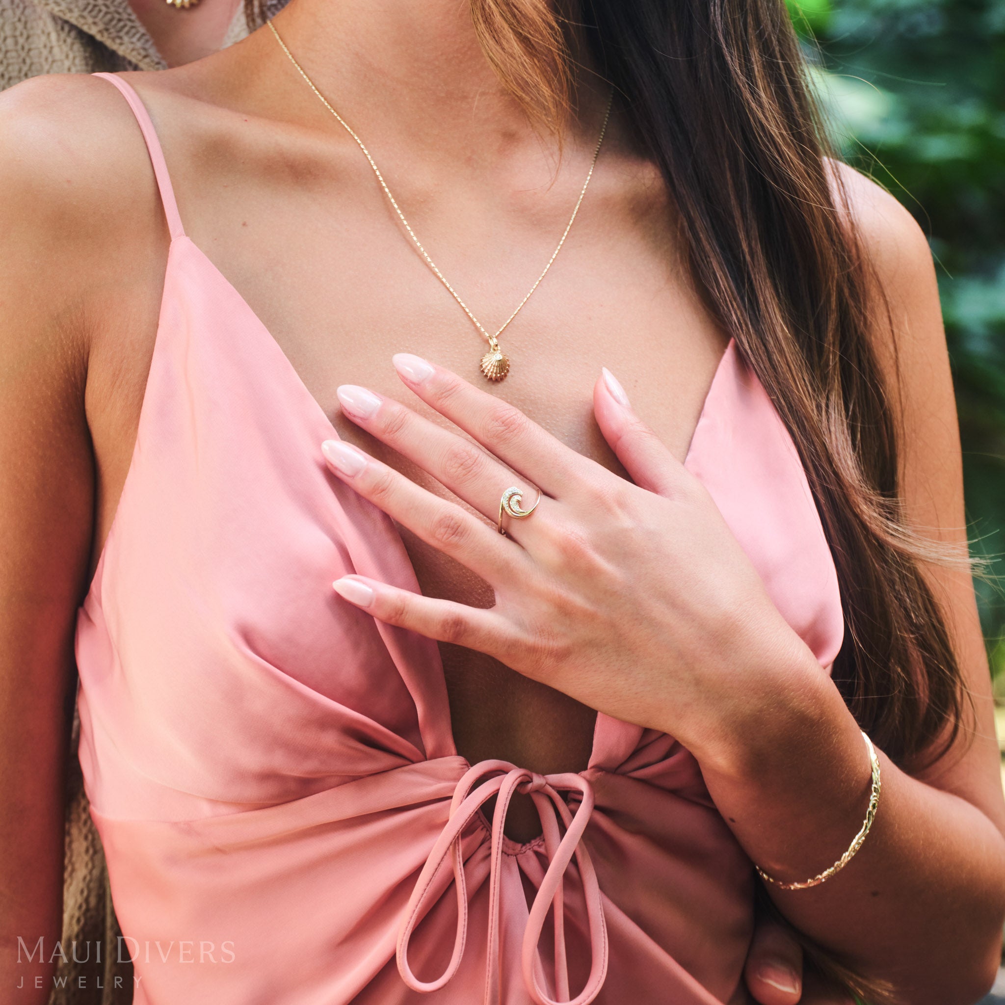 Close-up of a woman in a pink top wearing a Nalu Ring in 14k yellow gold with diamonds on her left hand