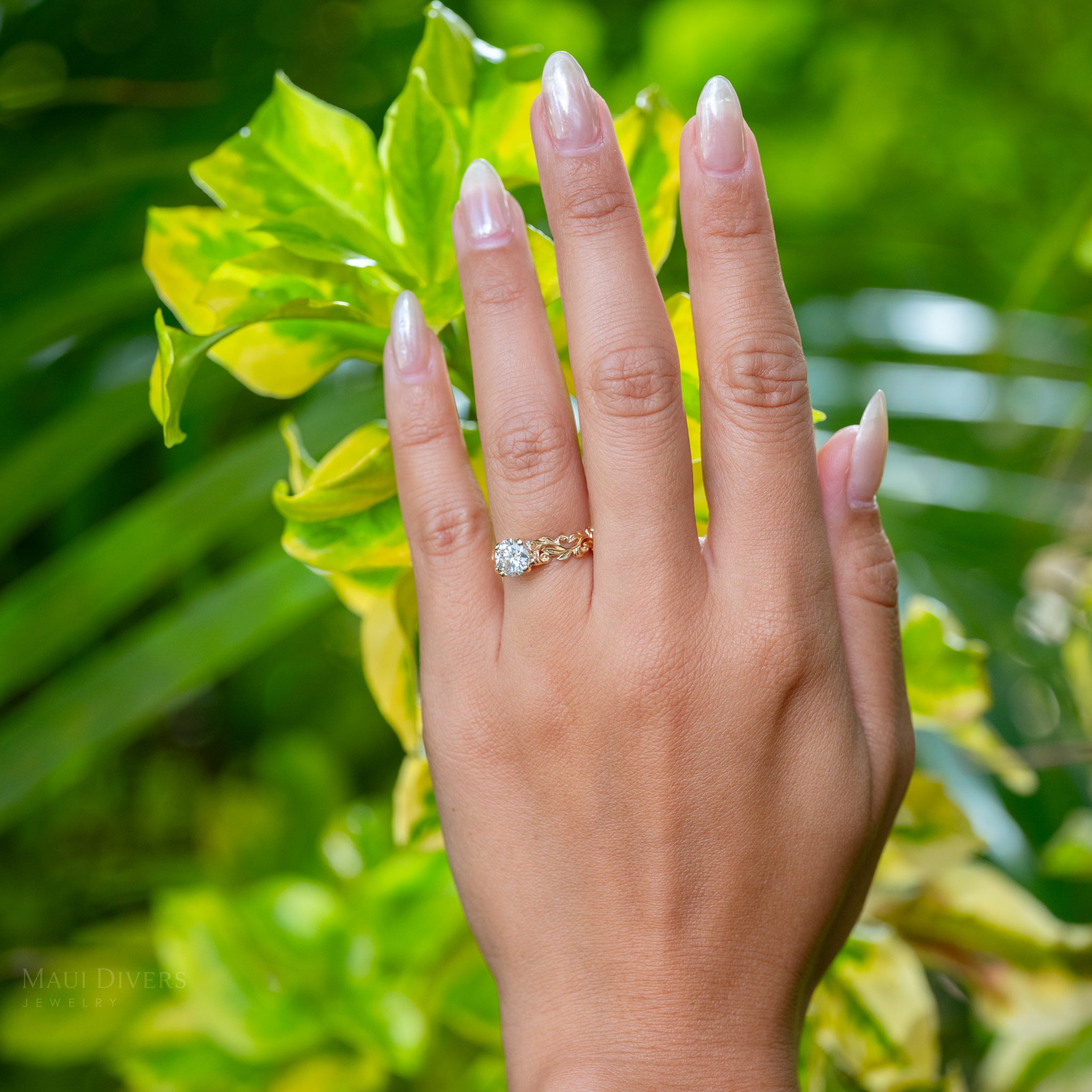 Hand wearing a 14k yellow gold Living Heirloom Engagement ring with a solitaire 2.02 carat lab grown diamond, set against a green leafy background
