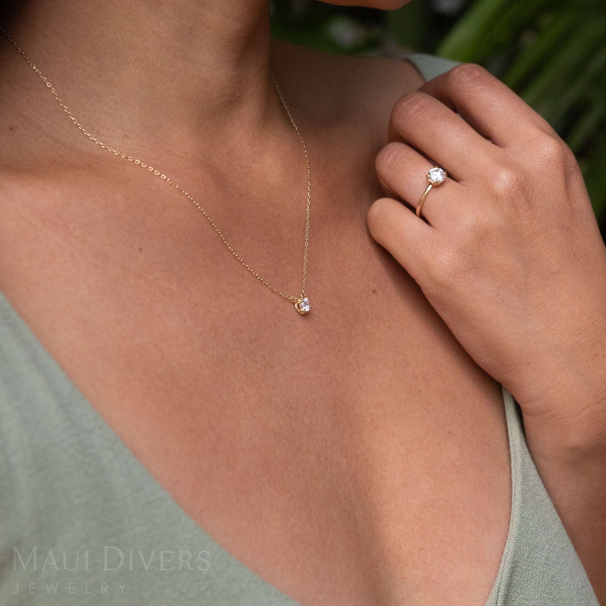 Close-up of a Woman in a Green Top Wearing an Adjustable Hidden Hawaiʻi Maile Necklace in 14k Yellow Gold with a Lab Grown Diamond Around Her Neck, with a Matching Ring on Her Left Hand