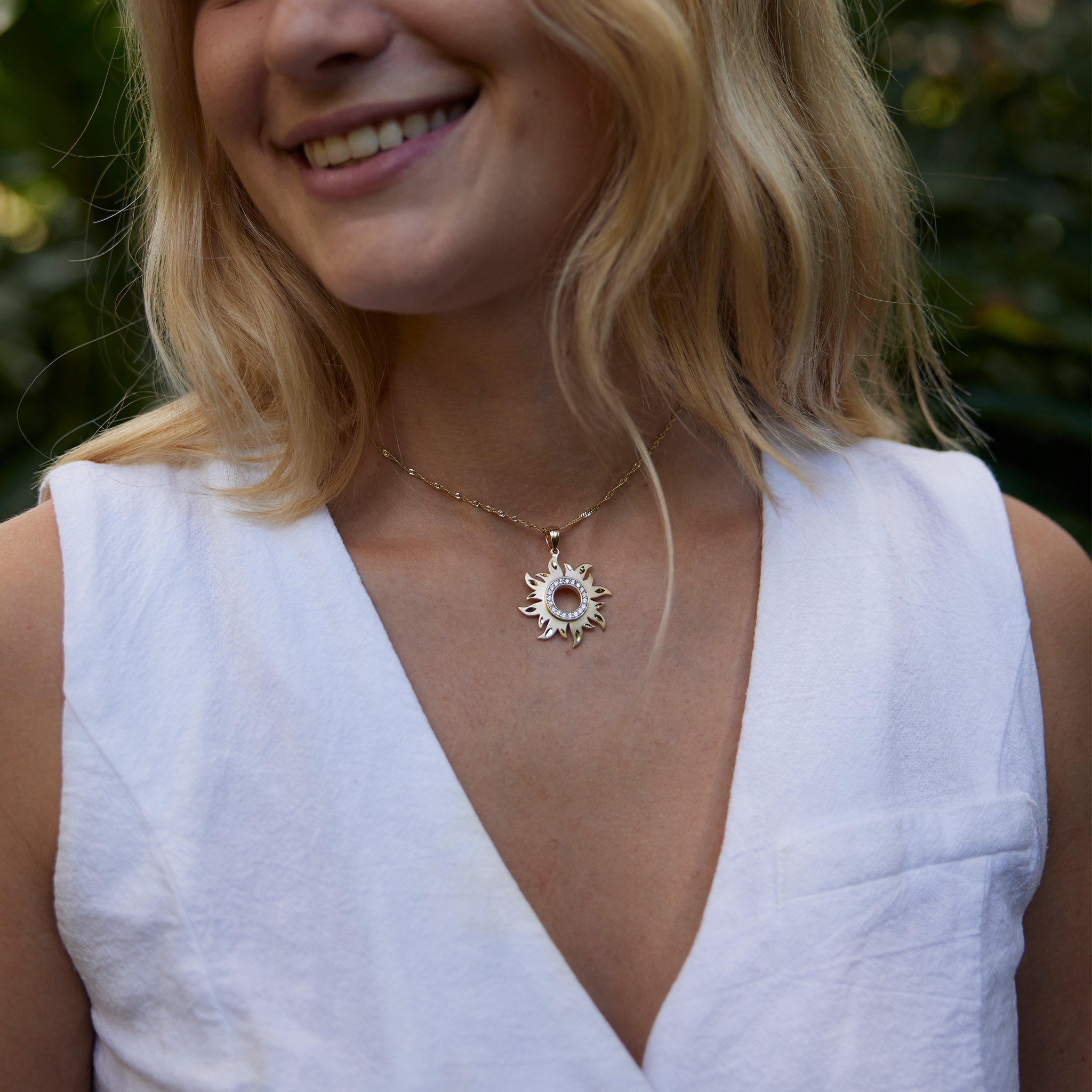 Woman in white shirt wearing Sun Pendant in Gold with Diamonds - 29mm with nature background