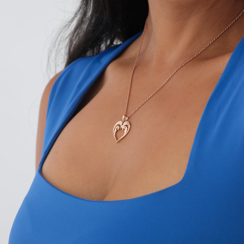 A woman's chest with a Nalu Heart Pendant in Rose Gold - 20mm - Maui Divers Jewelry