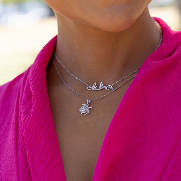A woman wearing a Honu Pendant in White Gold with Diamonds - 13mm and an Aloha necklace- Maui Divers Jewelry