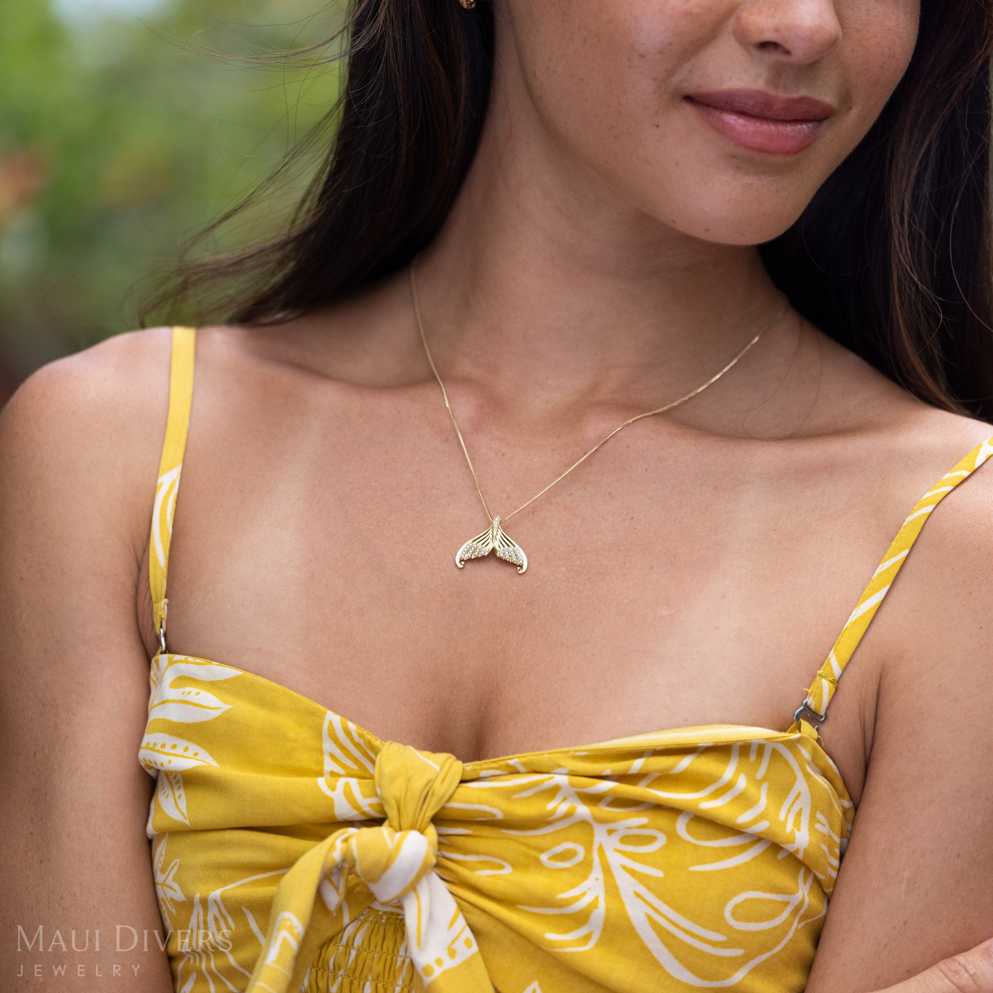 Close-up of a woman wearing a  Yellow Gold Mermaid Tail Necklace with Natural Diamond accents on a box chain and a yellow patterned top