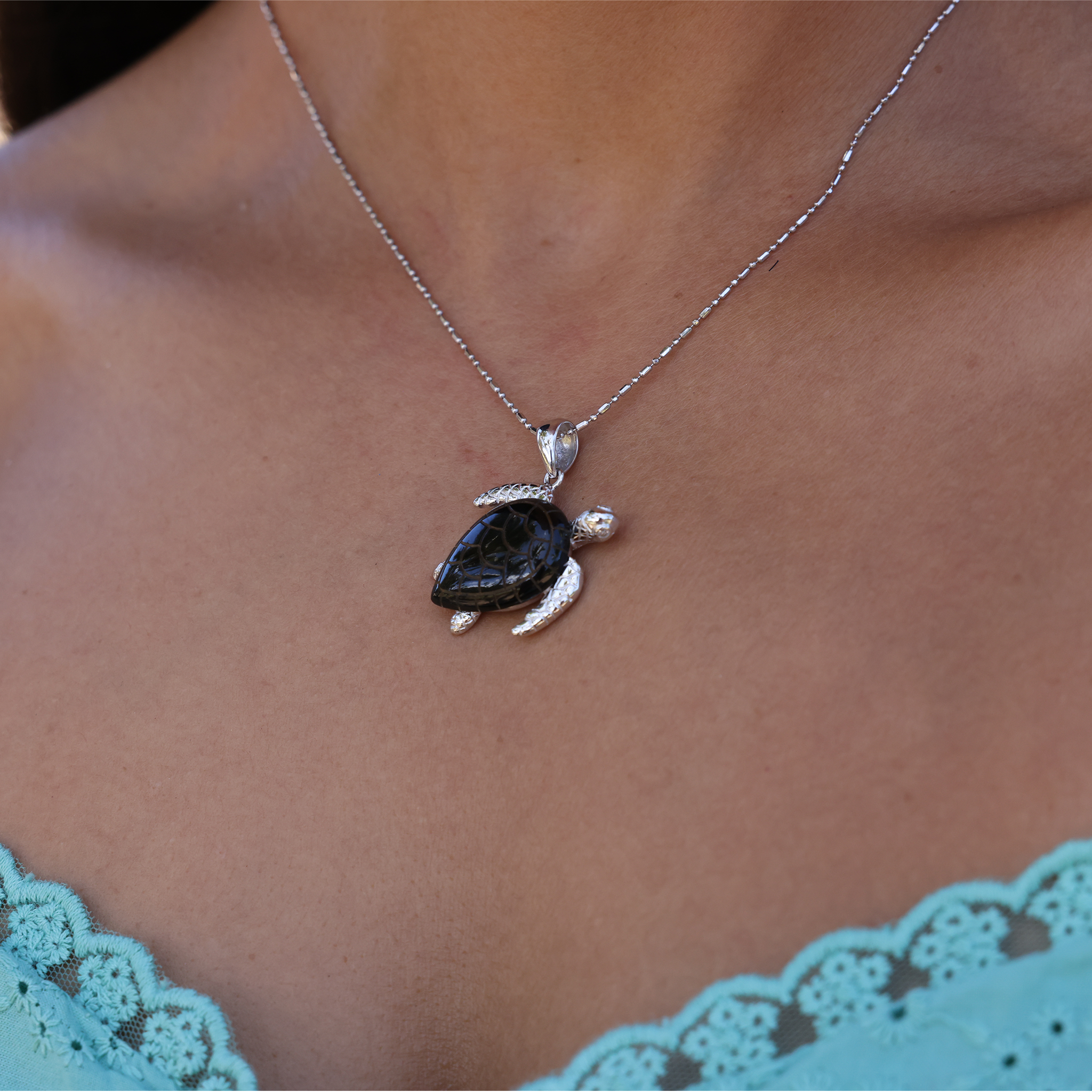 Maui Divers Jewelry Honu Black Coral Pendant in White Gold with Diamonds - 26mm on Chest with Teal Shirt
