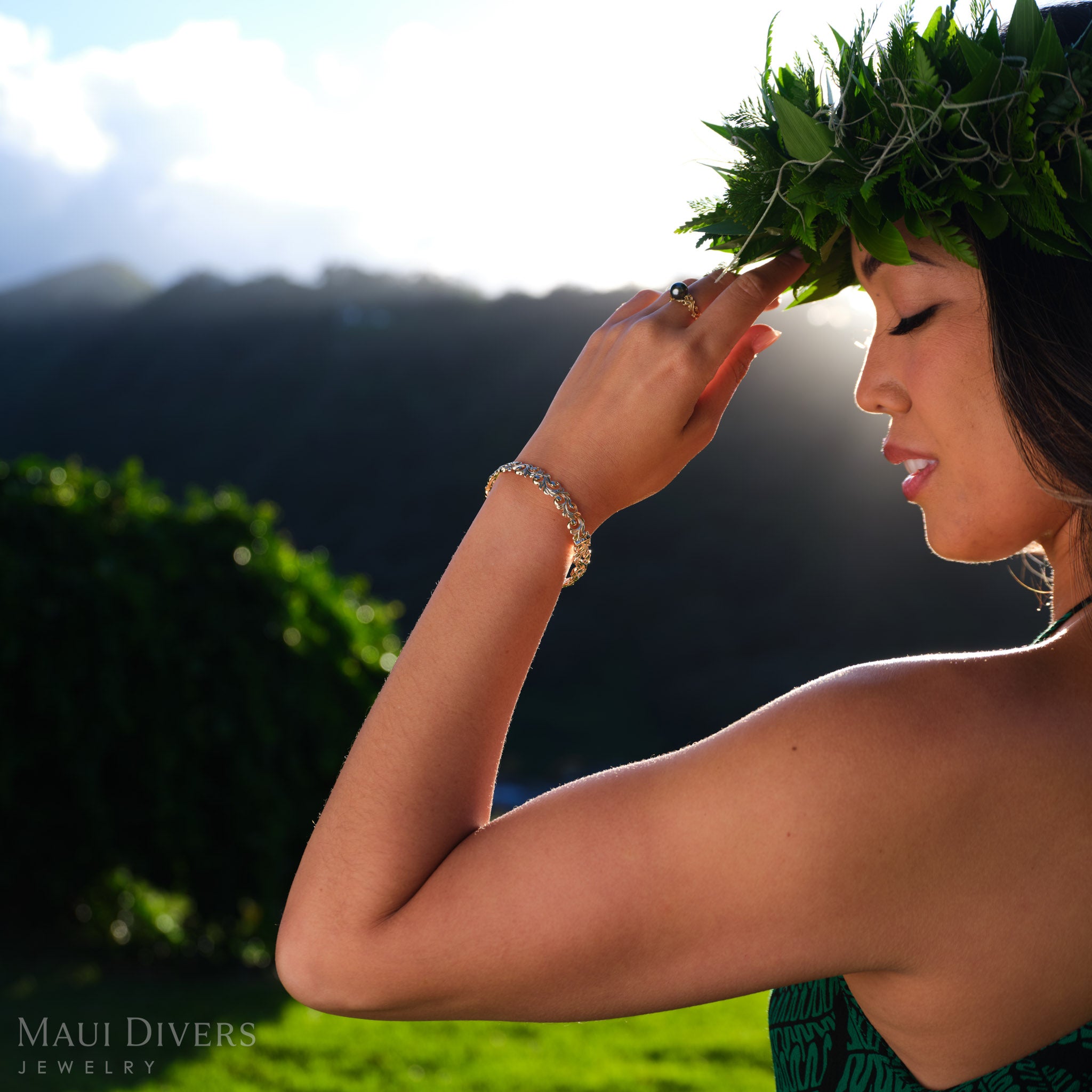Woman wearing a 14k yellow gold ring with a Tahitian black pearl and 14k yellow gold bracelet against a blurred outdoor background