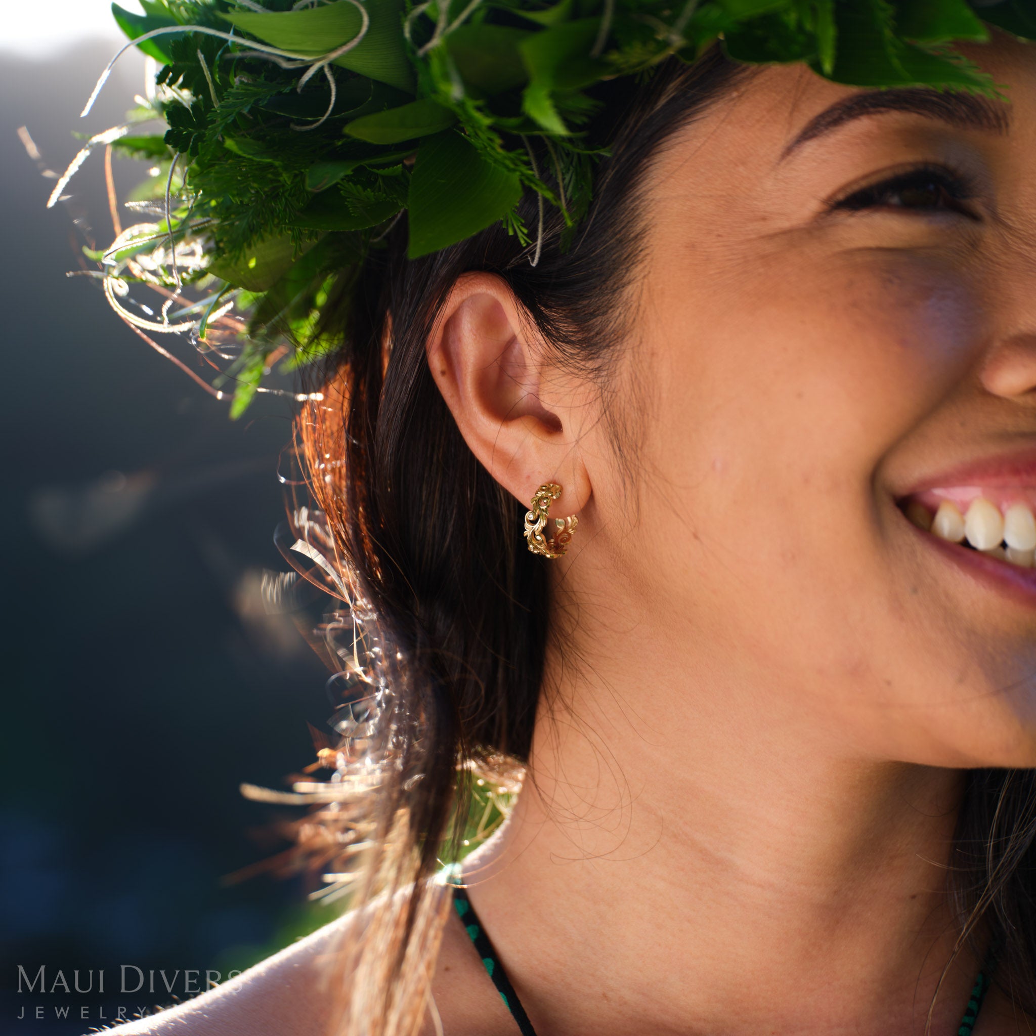 Smiling woman in a leafy headpiece wearing a Living Heirloom hoop earring in 14k yellow gold with diamond accents