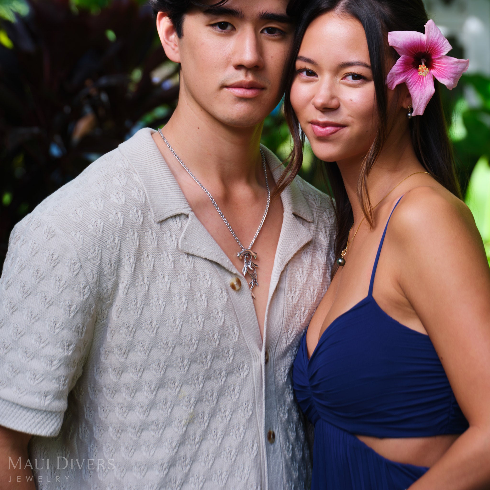 Smiling man and woman standing close together, with the man wearing a Living Heirloom Hammerhead Shark Pendant in sterling silver around his neck and the woman wearing a Tahitian black pearl pendant in 14k yellow gold around her neck