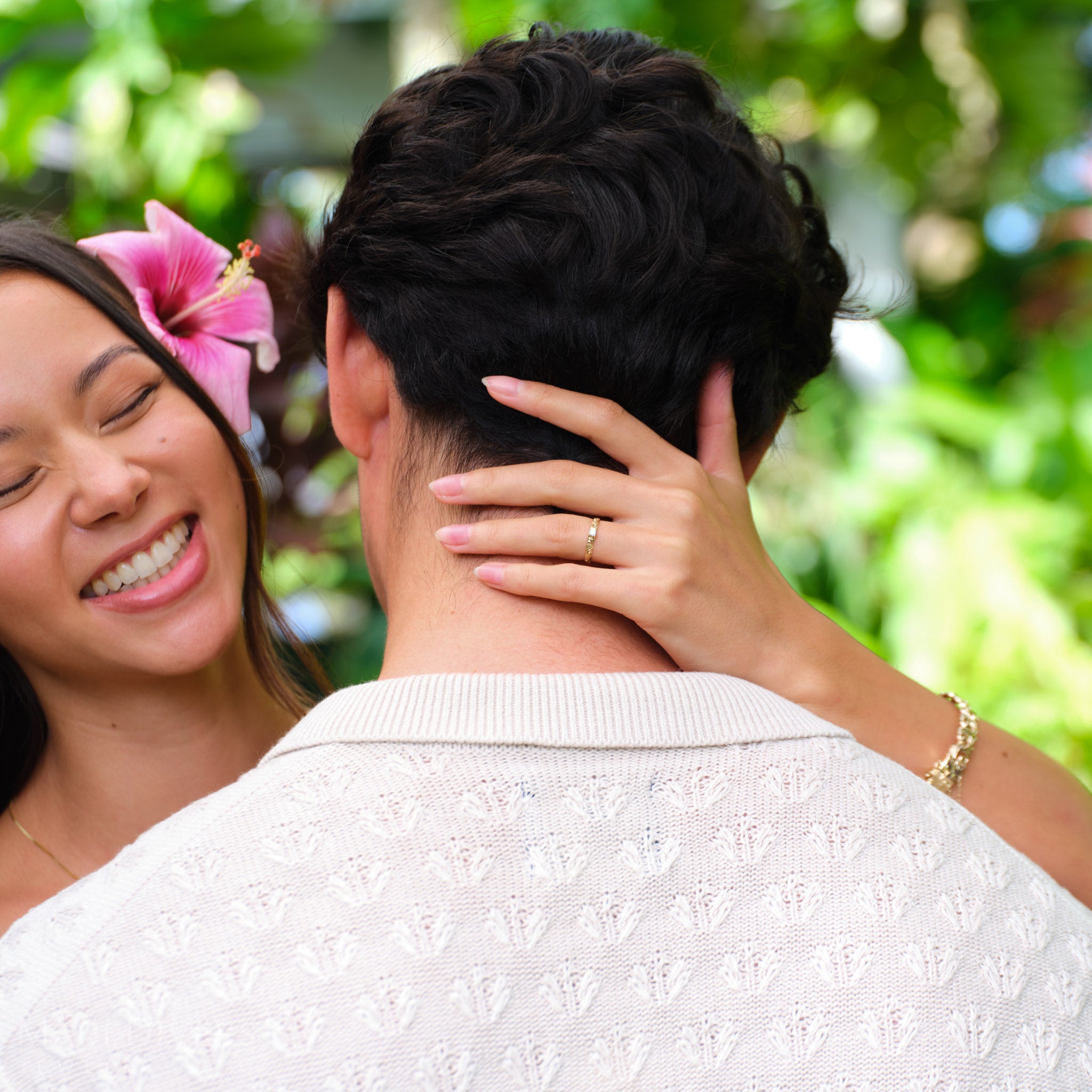 Smiling woman wearing a Living Heirloom Ring in 14k yellow gold with a diamond on her ring finger, touching the back of a man's neck against a blurred outdoor background