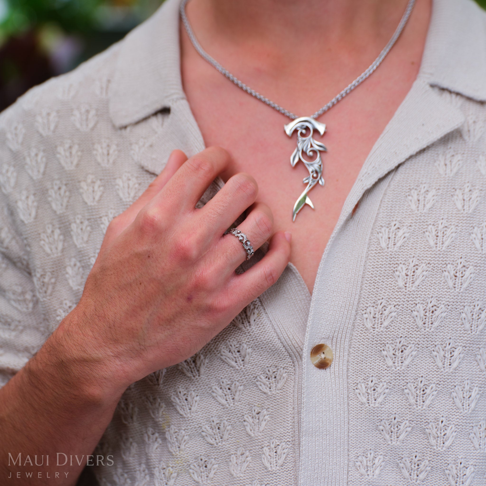Close-up of a person wearing a Living Heirloom Ring in 14k white gold with diamond accents, holding the collar of a tan shirt, with a blurred Living Heirloom Hammerhead Shark Pendant visible on their chest