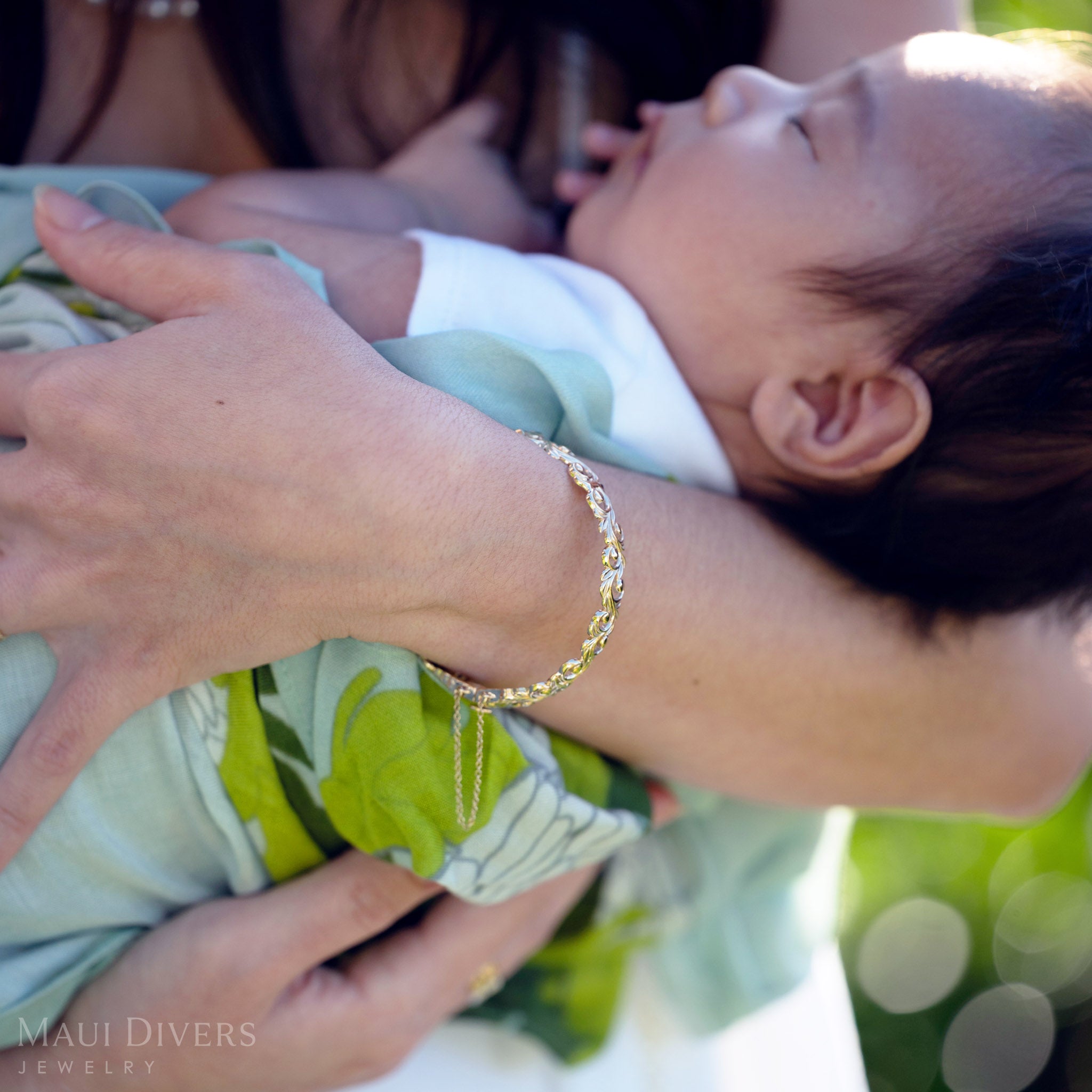 Close-up of a Living Heirloom Hinge Bracelet in 14k yellow gold worn on the left wrist, with an arm wrapped around a baby