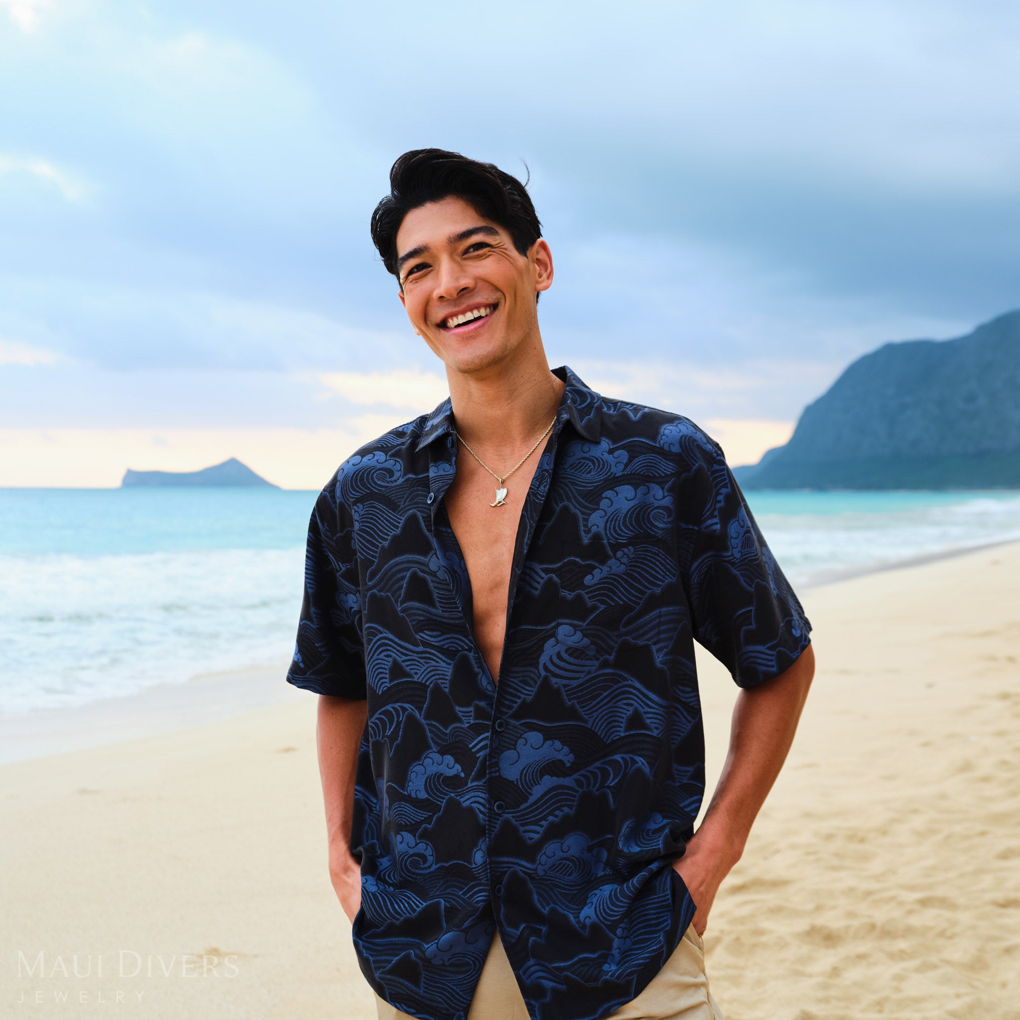 Waʻa (Canoe) Pendant on a gold chain worn by a man in a blue patterned shirt on a beach