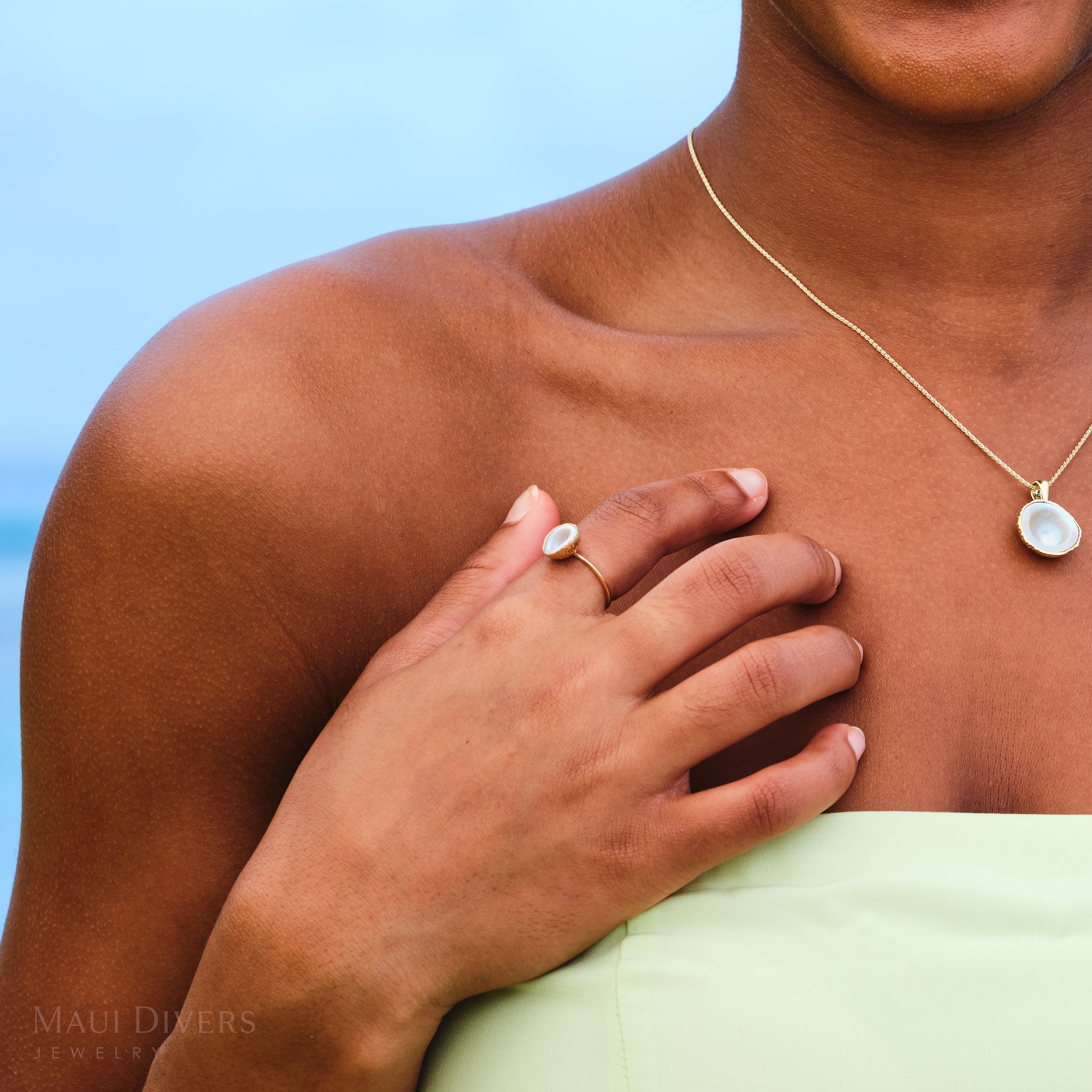 Person wearing a coconut mother of pearl ring in 14k yellow gold with a blue background