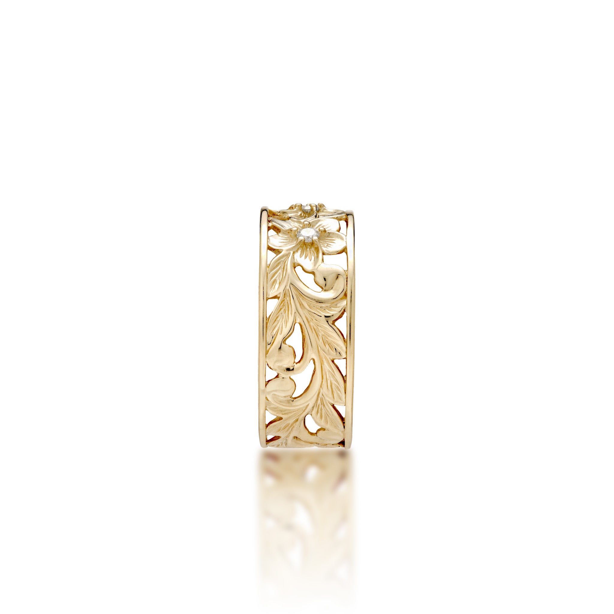 A side view of a 14k yellow gold Hawaiian Heirloom ring with an intricate fern and maile leaf scrollwork pattern featuring plumeria flowers at the top with diamond accents, shown on a clean white background with a soft reflection.