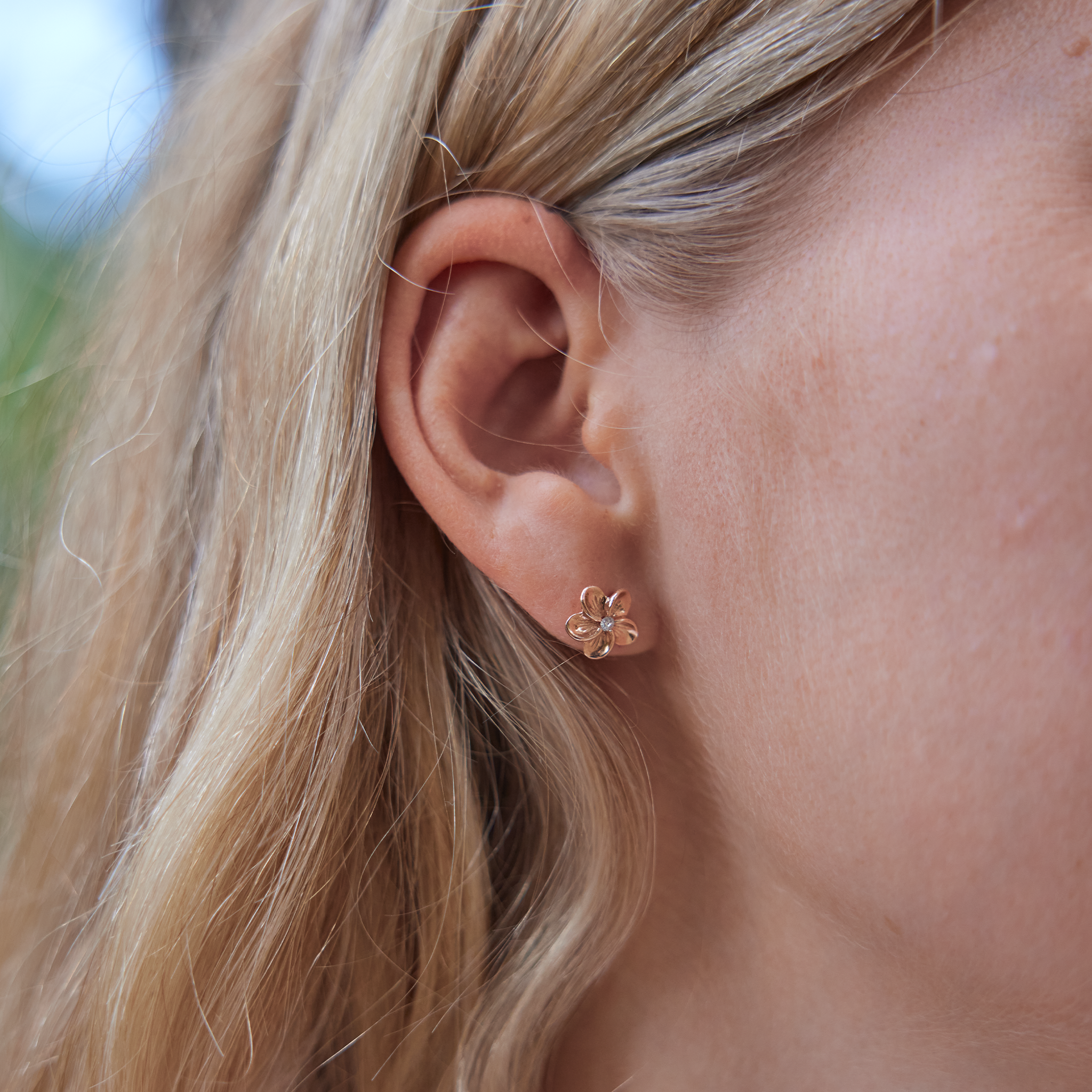 Womanʻs right ear with Hawaiian Heirloom Plumeria Earrings in Rose Gold with Diamonds