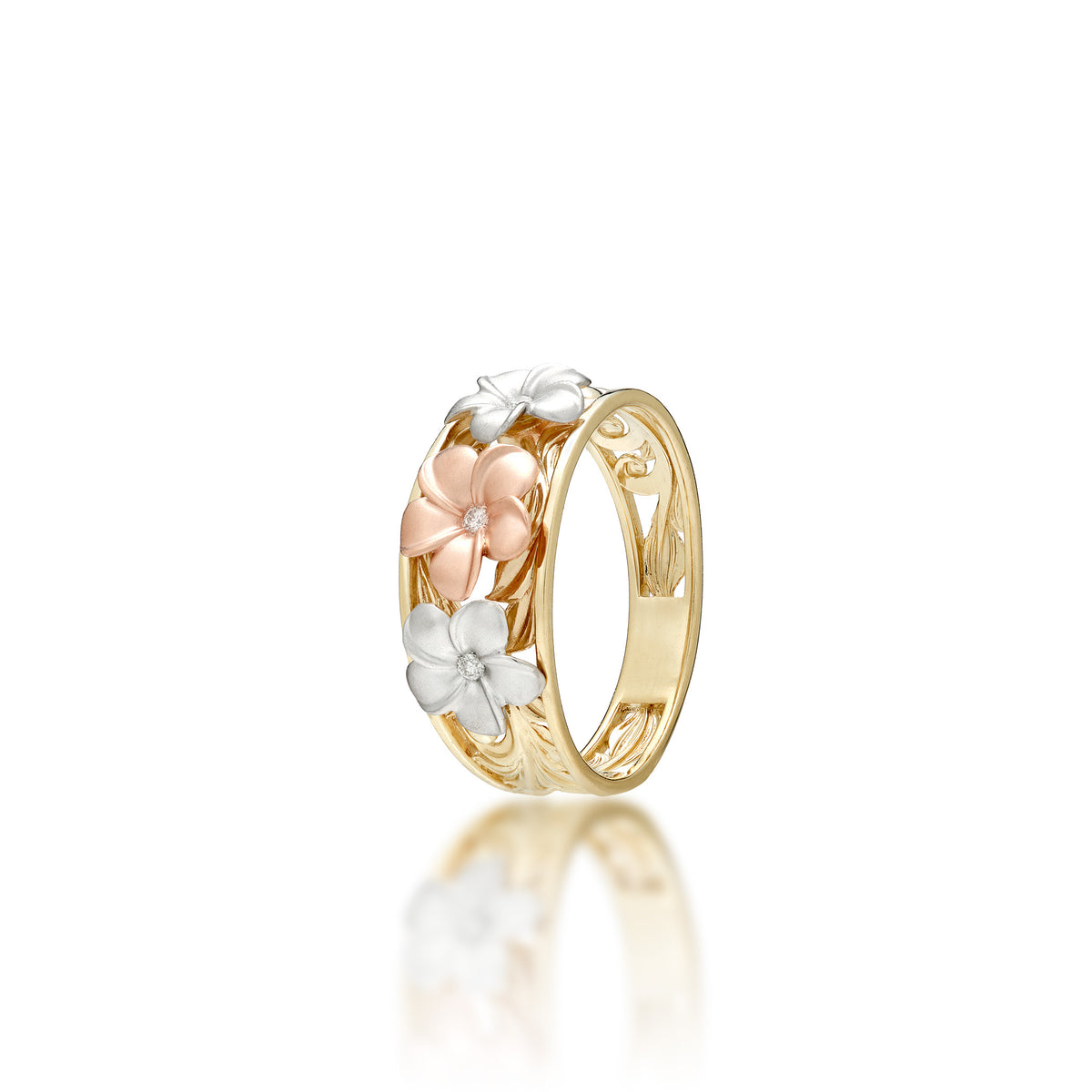 A Hawaiian Heirloom Ring with a 14k yellow gold band featuring hāpuʻu fern and maile leaf scrollwork and a single 14k diamond-accented rose gold plumeria at the top and a 14k white gold diamond-accented plumeria on each side, shown on a white background