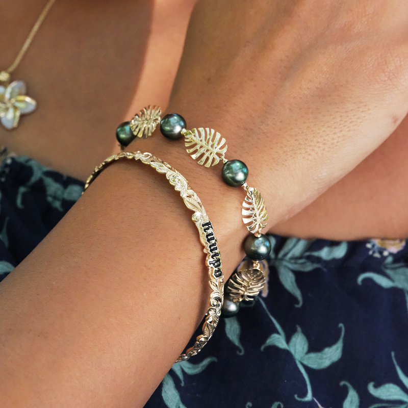 A woman's wrist with a Hawaiian Heirloom Kuuipo (Sweetheart) Plumeria Enamel Bracelet in Gold - 6mm - Maui Divers Jewelry