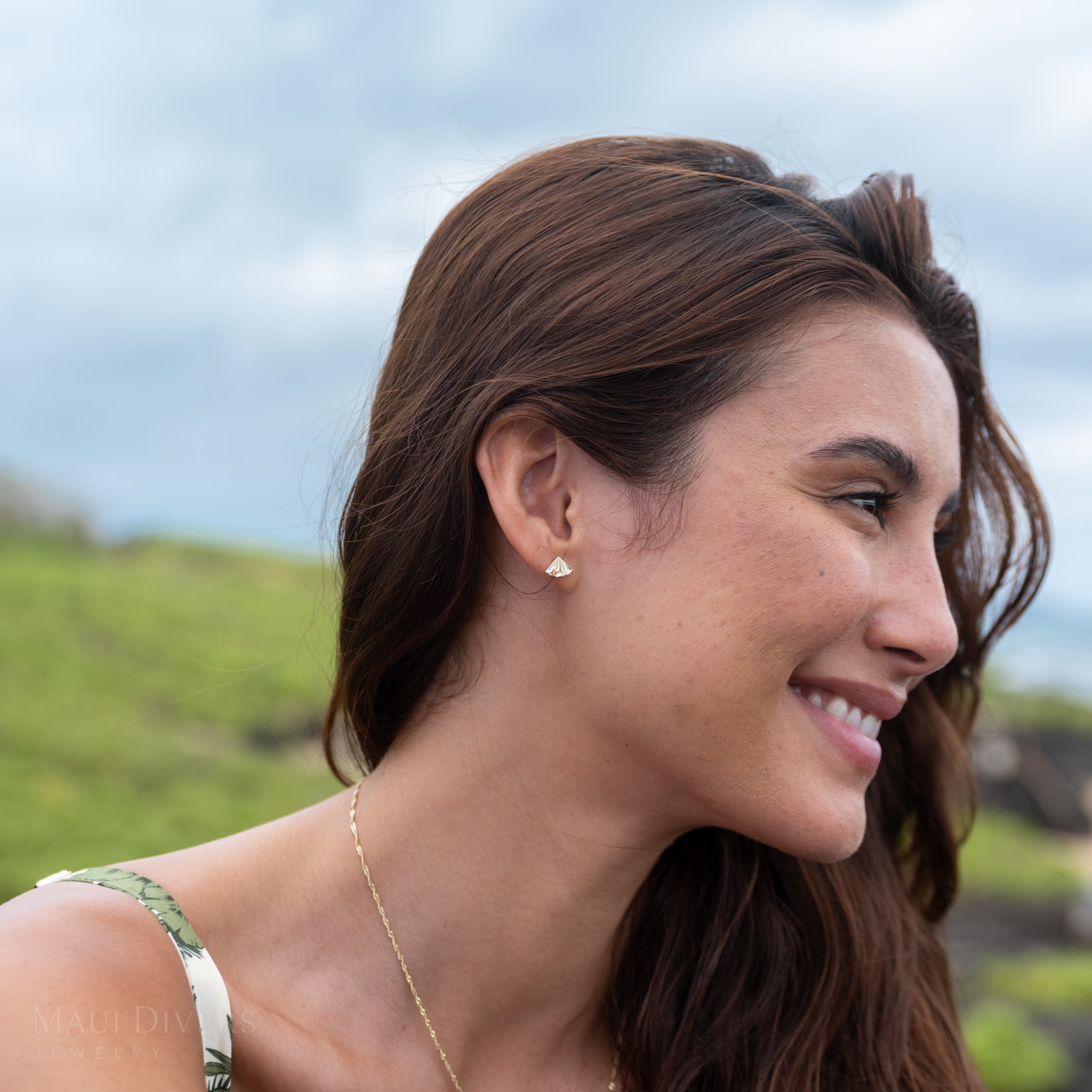 Woman with a side profile smile in a natural setting wearing a gold and orange sapphire pineapple earring