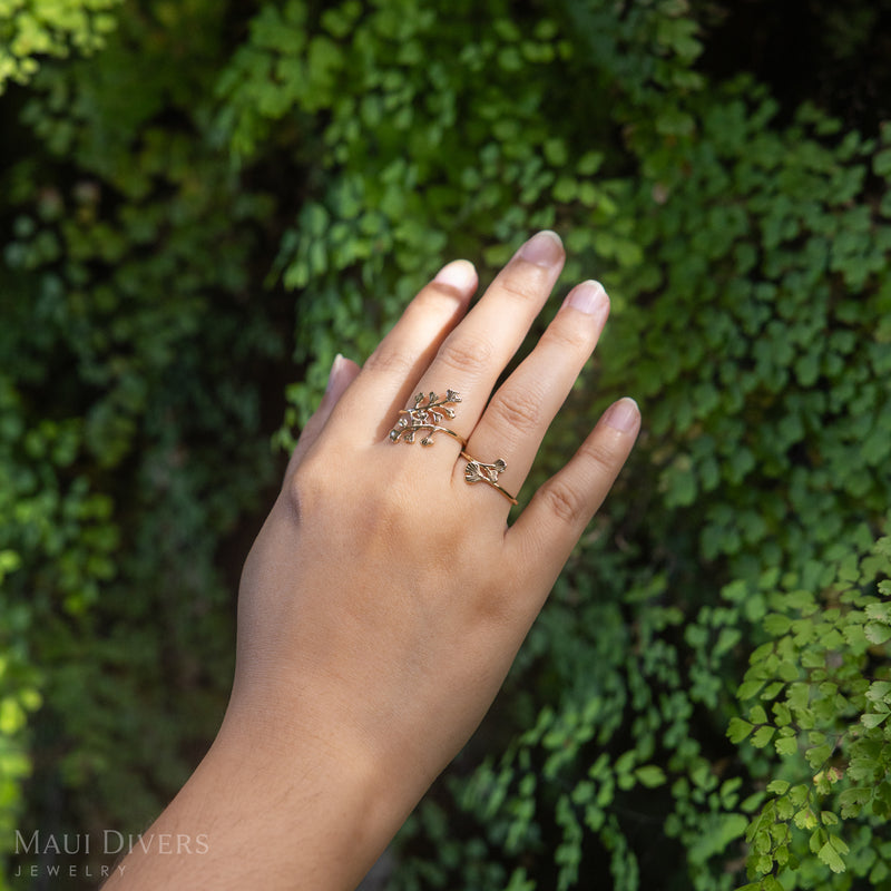 Hand wearing a 14k yellow gold Maiden Hair ring with blurry green maiden hair ferns in the background