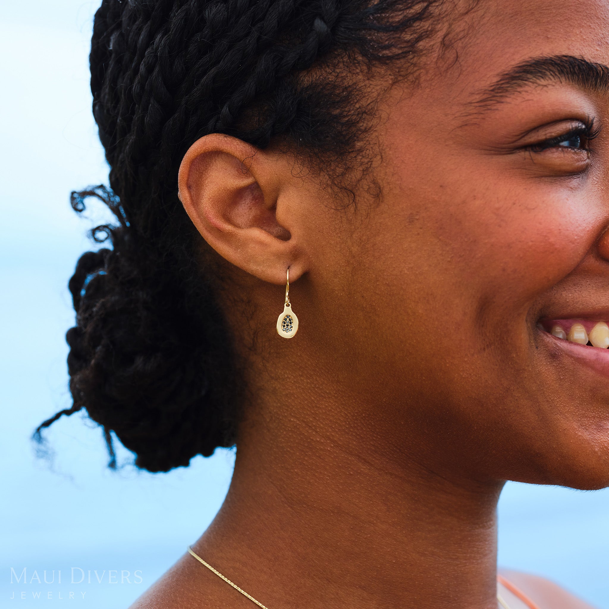 Close-up side view of a smiling woman wearing a Cute Fruits Papaya Earring with black diamonds in 14k yellow gold on her right ear