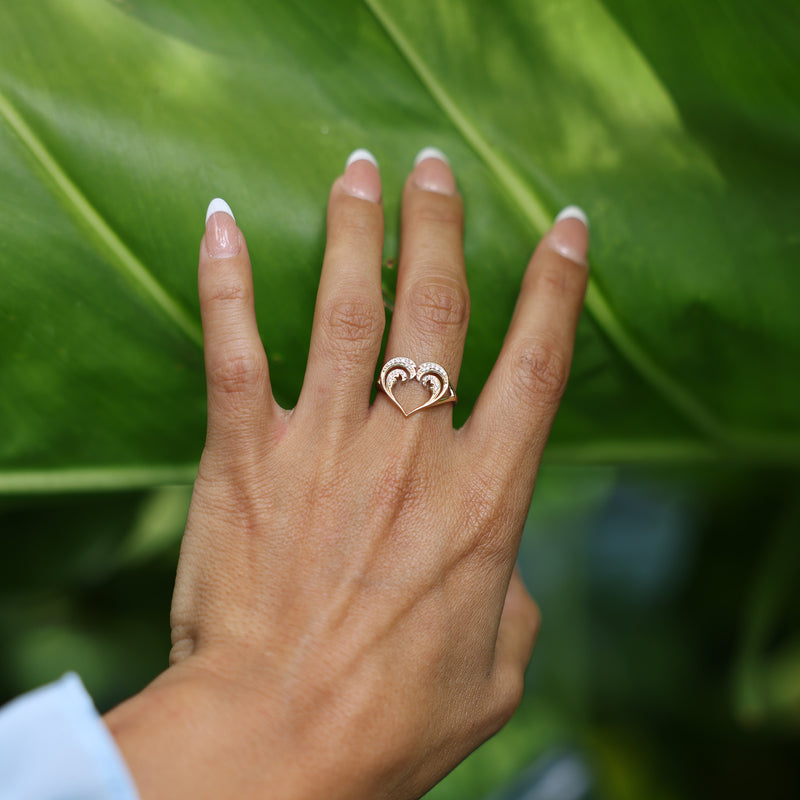 Close up of Nalu Heart Ring in Gold with Diamonds on Woman's Hand touching leaf