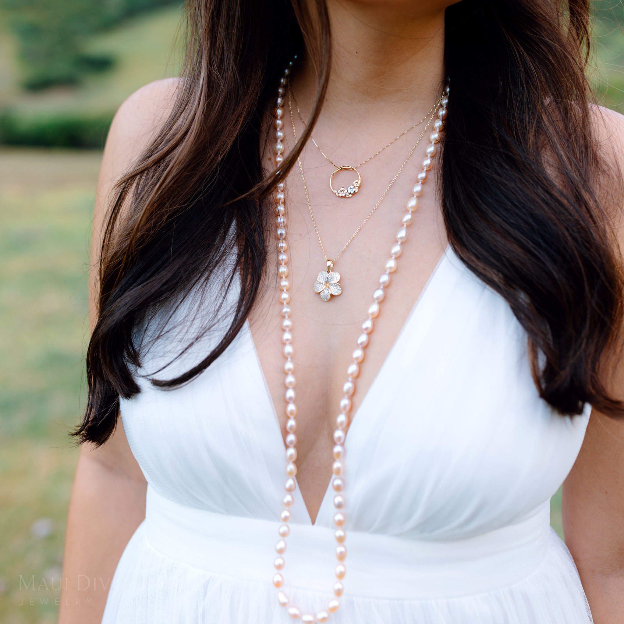 Woman wearing a white dress with a long peach pearl necklace and plumeria pendants