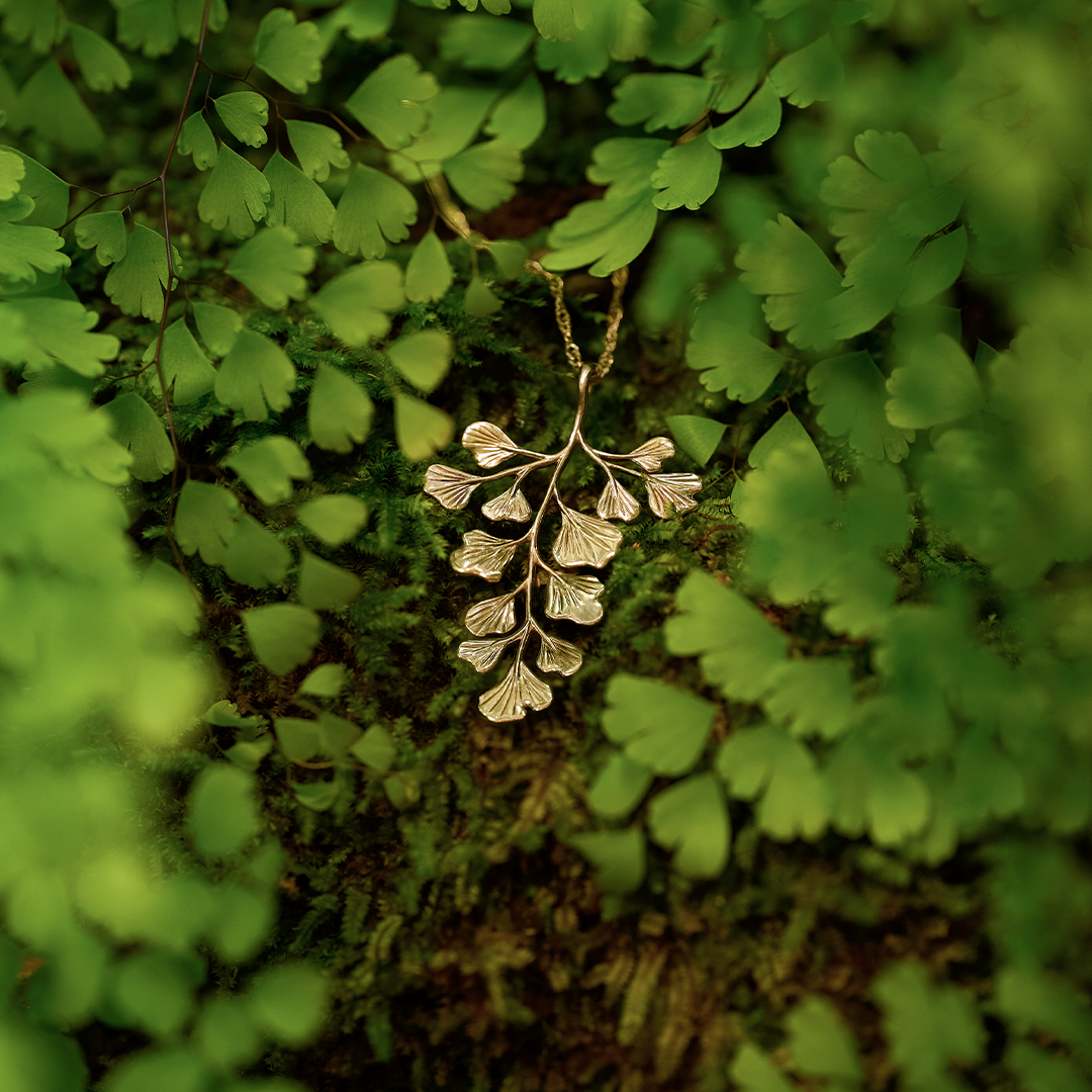 ʻIwaʻiwa (Maiden Hair) Pendant in 14k yellow gold resting on moss with maiden hair ferns around it  