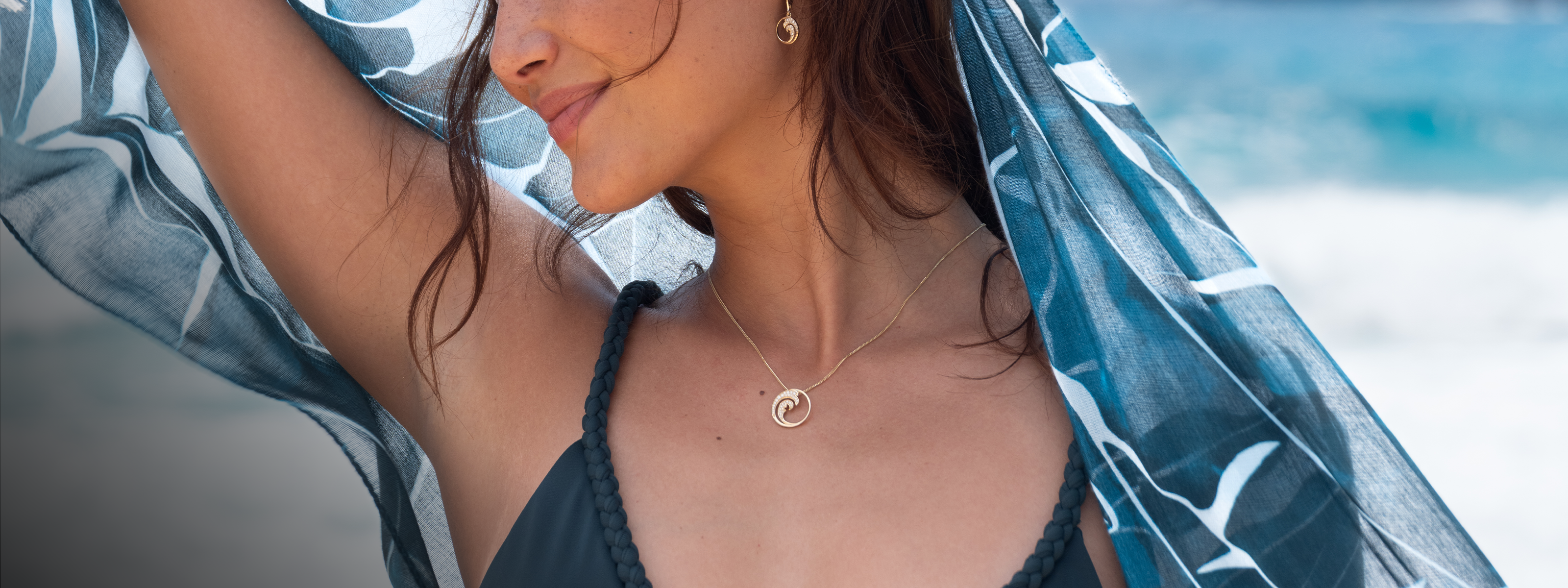 Woman wearing a Nalu (Wave) Diamond Pendant on a chain by the beach