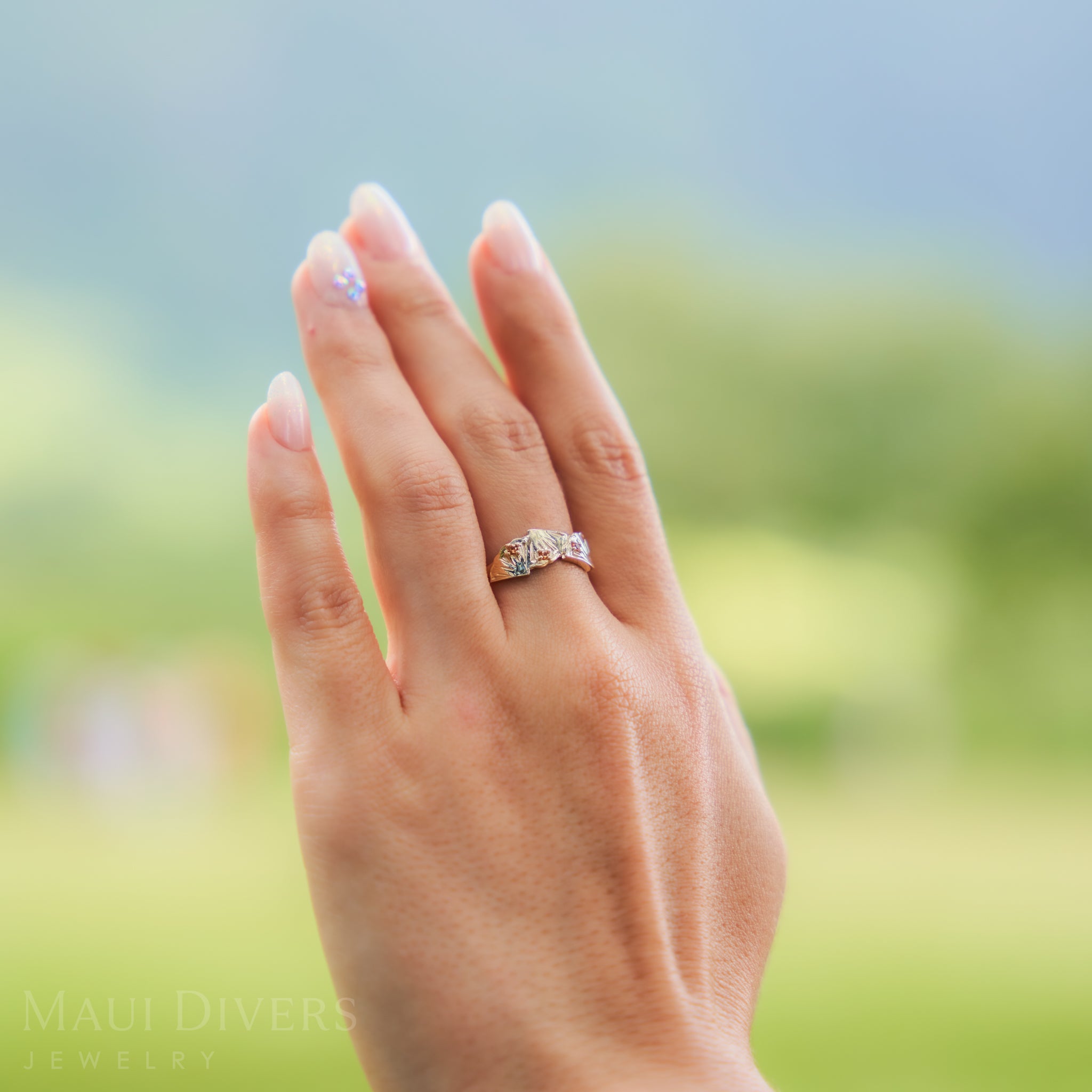 Hand wearing a pineapple ring with a blurred green background