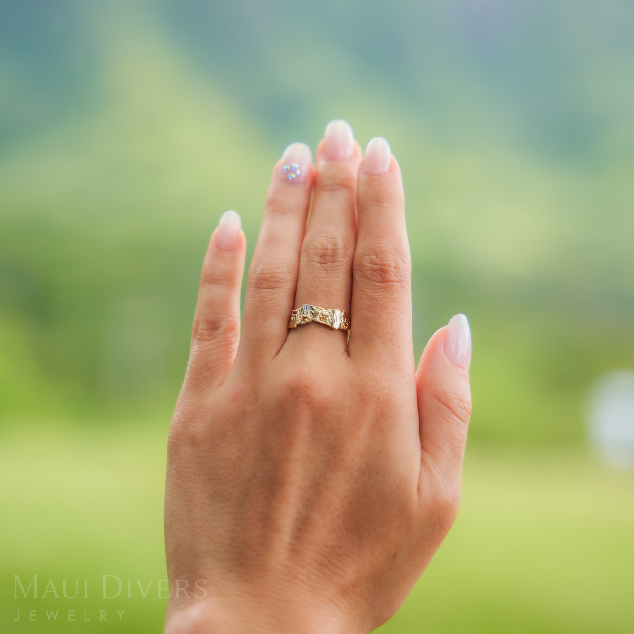 Hand wearing a pineapple ring with a blurred green background