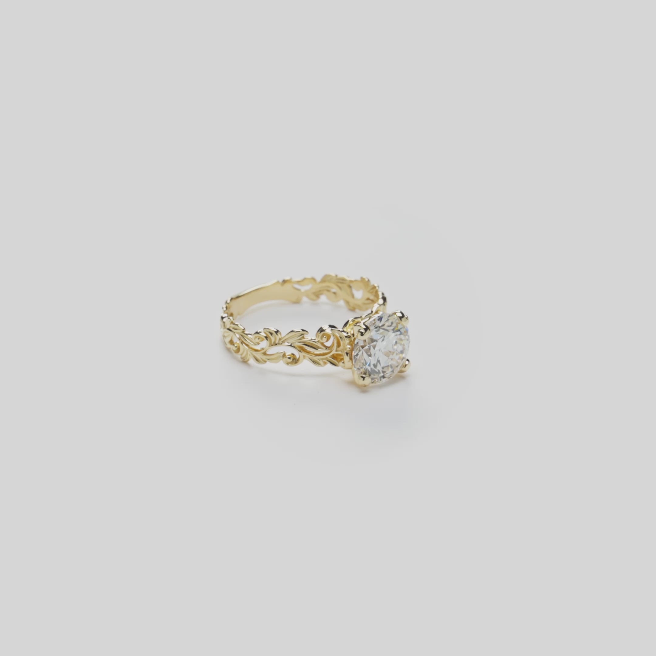 Video showcasing a 14k Yellow Gold Living Heirloom Collection Engagement Ring with maile leaf and hāpuʻu fern scrollwork and a solitaire 2.02 carat round brilliant diamond at the crown, shown on a white background with a soft reflection