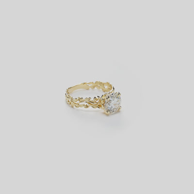 Video showcasing a 14k Yellow Gold Living Heirloom Collection Engagement Ring with maile leaf and hāpuʻu fern scrollwork and a solitaire 2.02 carat round brilliant diamond at the crown, shown on a white background with a soft reflection
