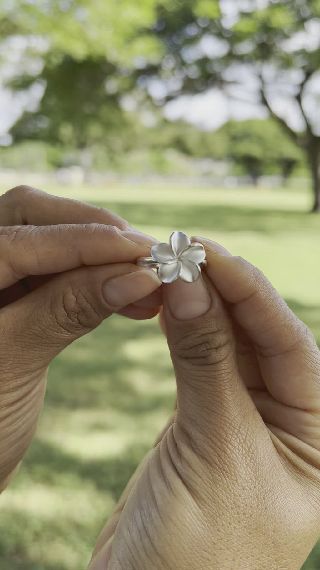 Video of 	a woman's hand holding a Plumeria Ring in Sterling Silver - 15mm by Maui Divers Jewelry and a bracelet.