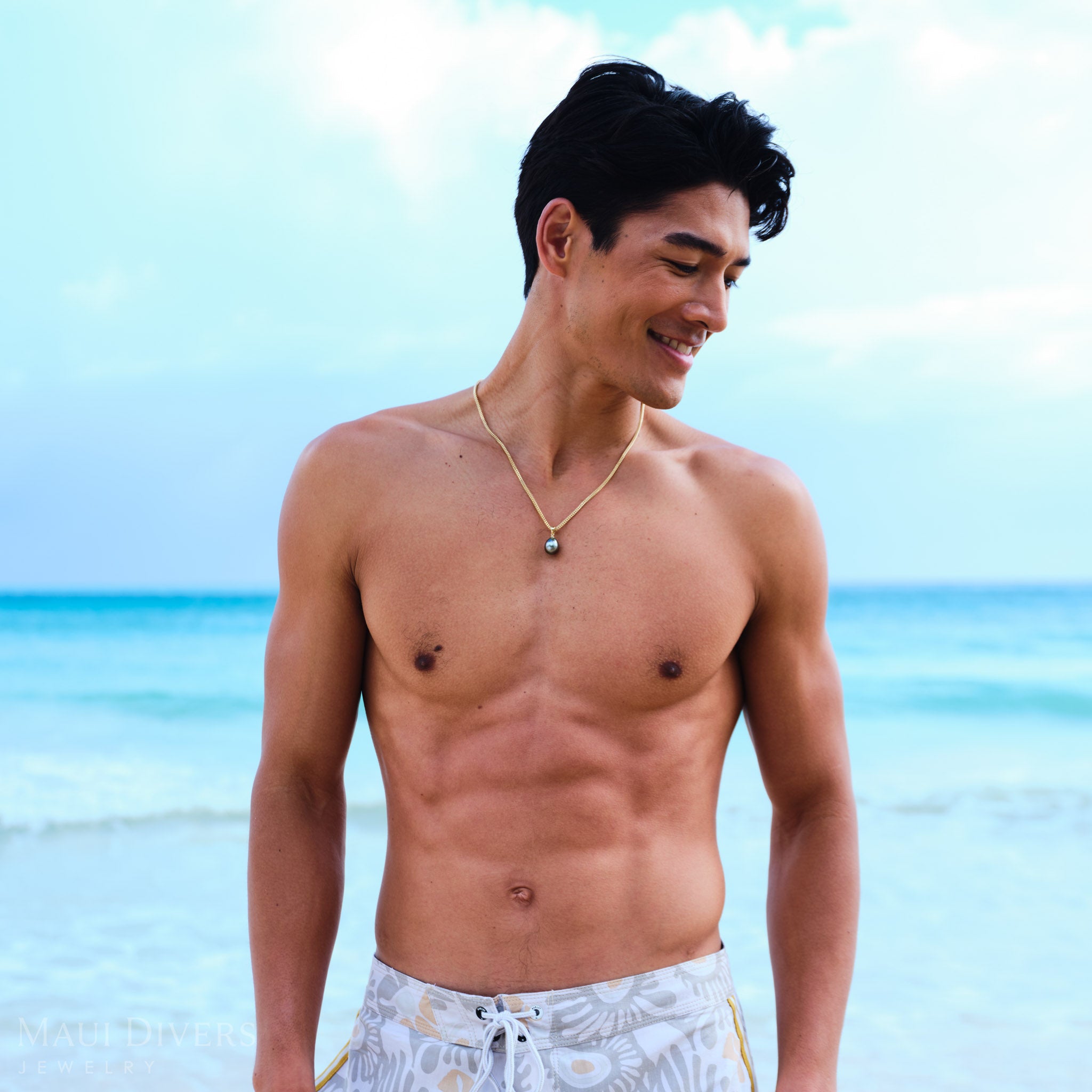 Man wearing a gold necklace with a Tahitian black pearl pendant pendant on a beach