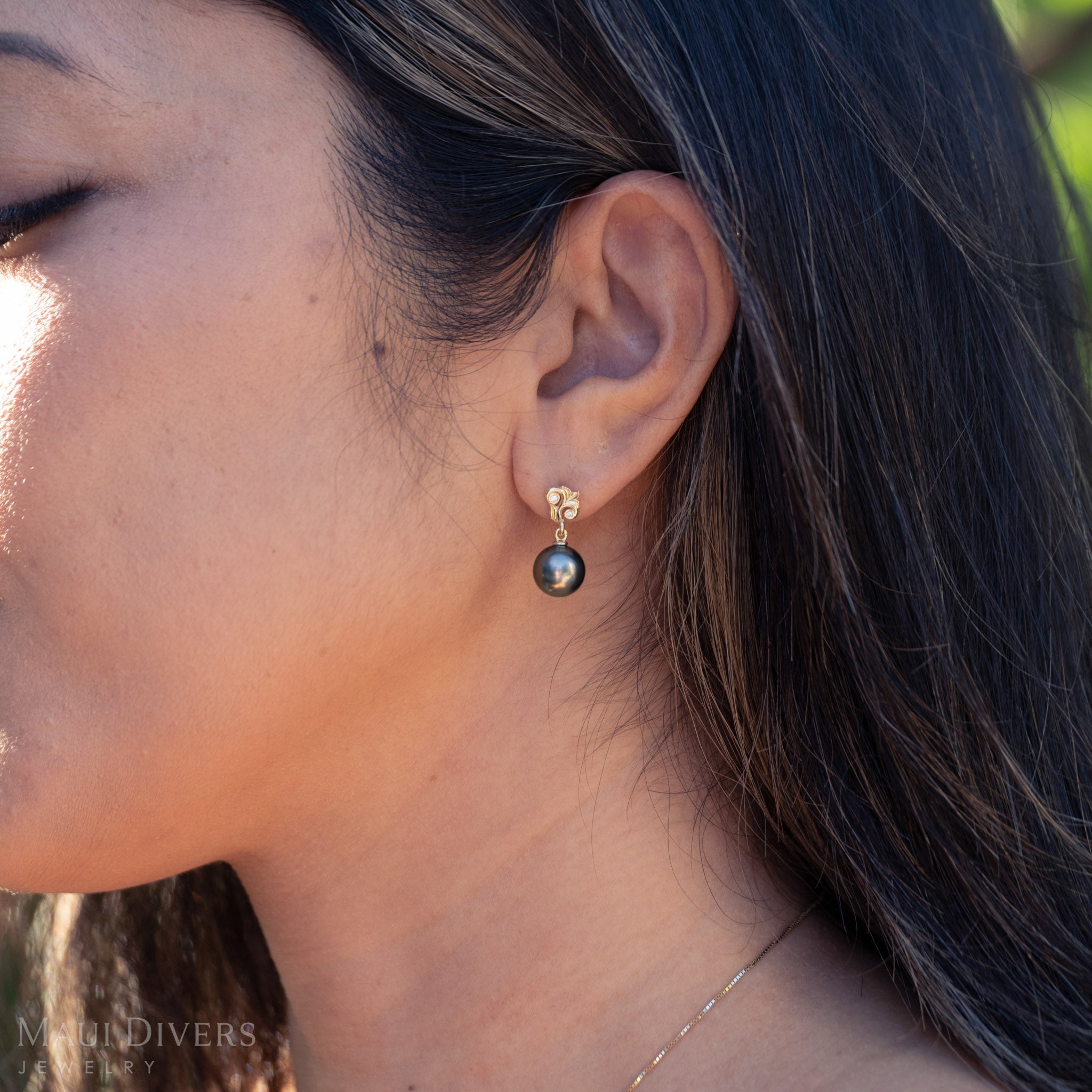 Close-up of a person wearing a black pearl earring with a blurred background