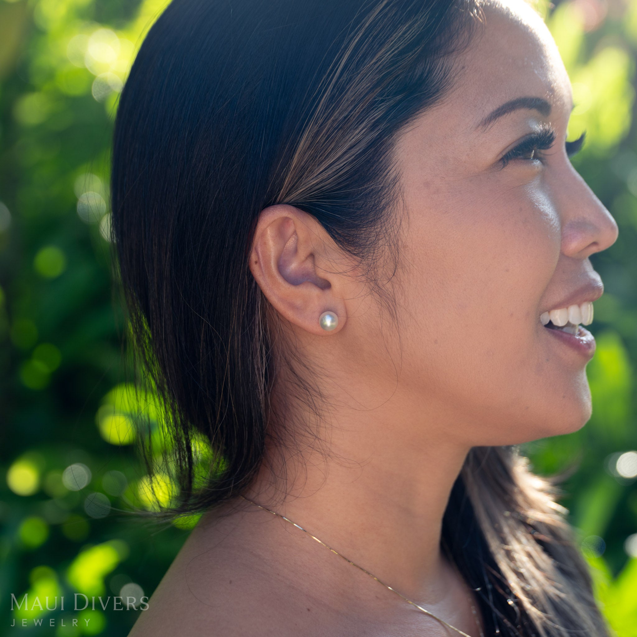 Woman wearing a South Sea white pearl earring with a blurred green background