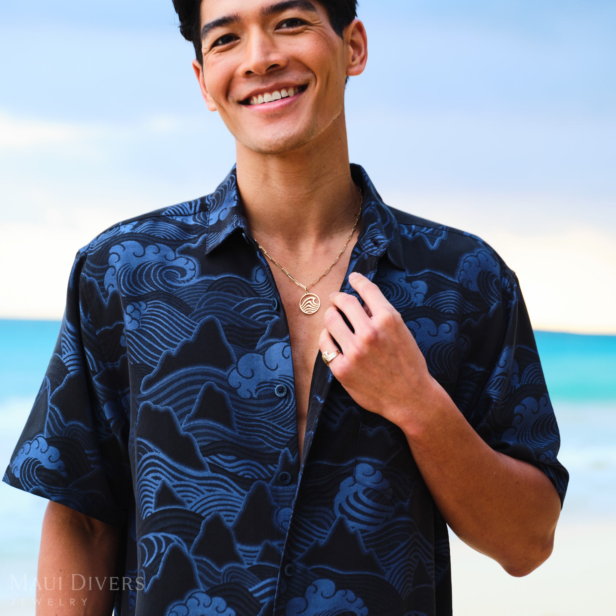 Man wearing a Modern style wave pendant and ring with blue patterned shirt on a beach