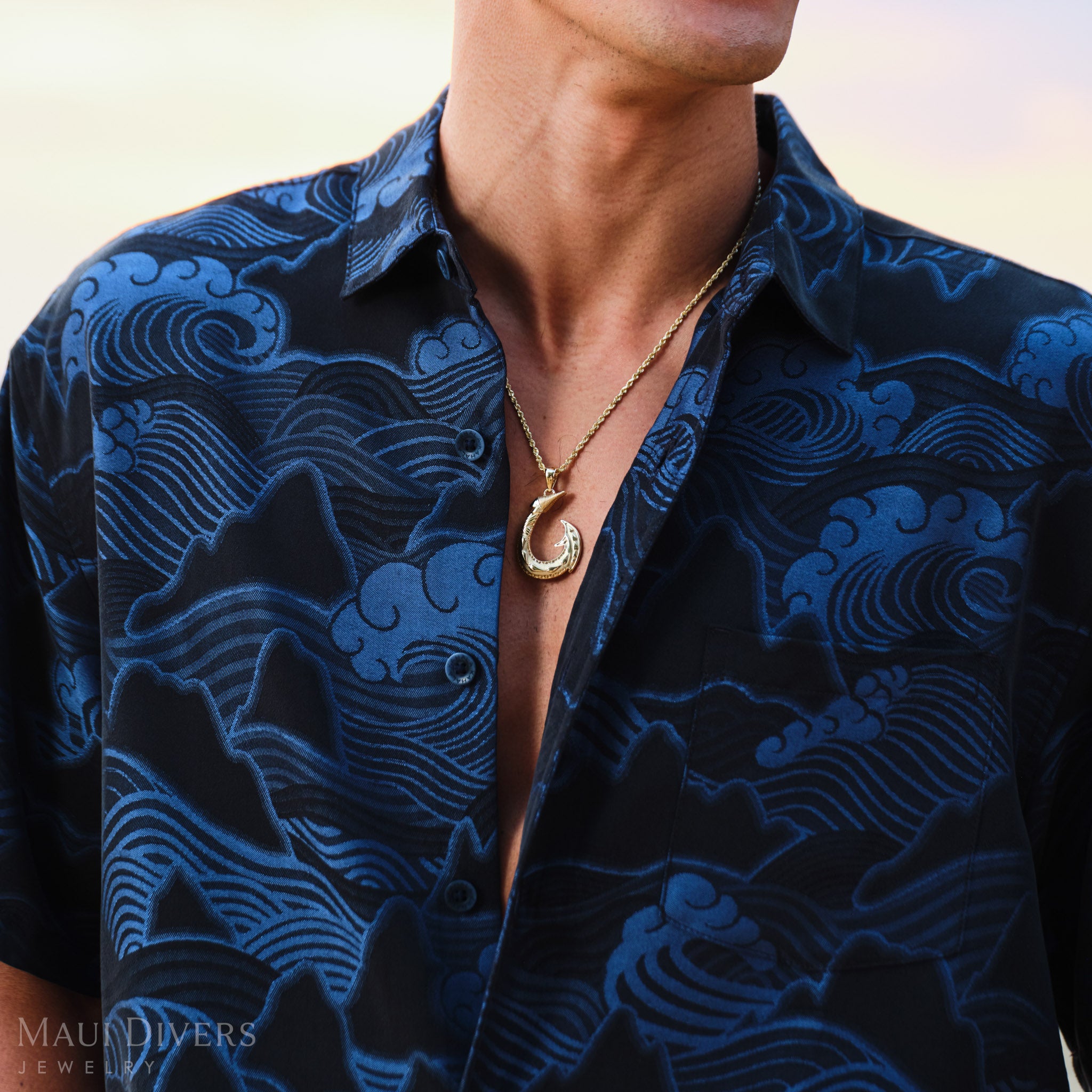 Man wearing a blue patterned shirt with a Hawaiian fish hook pendant