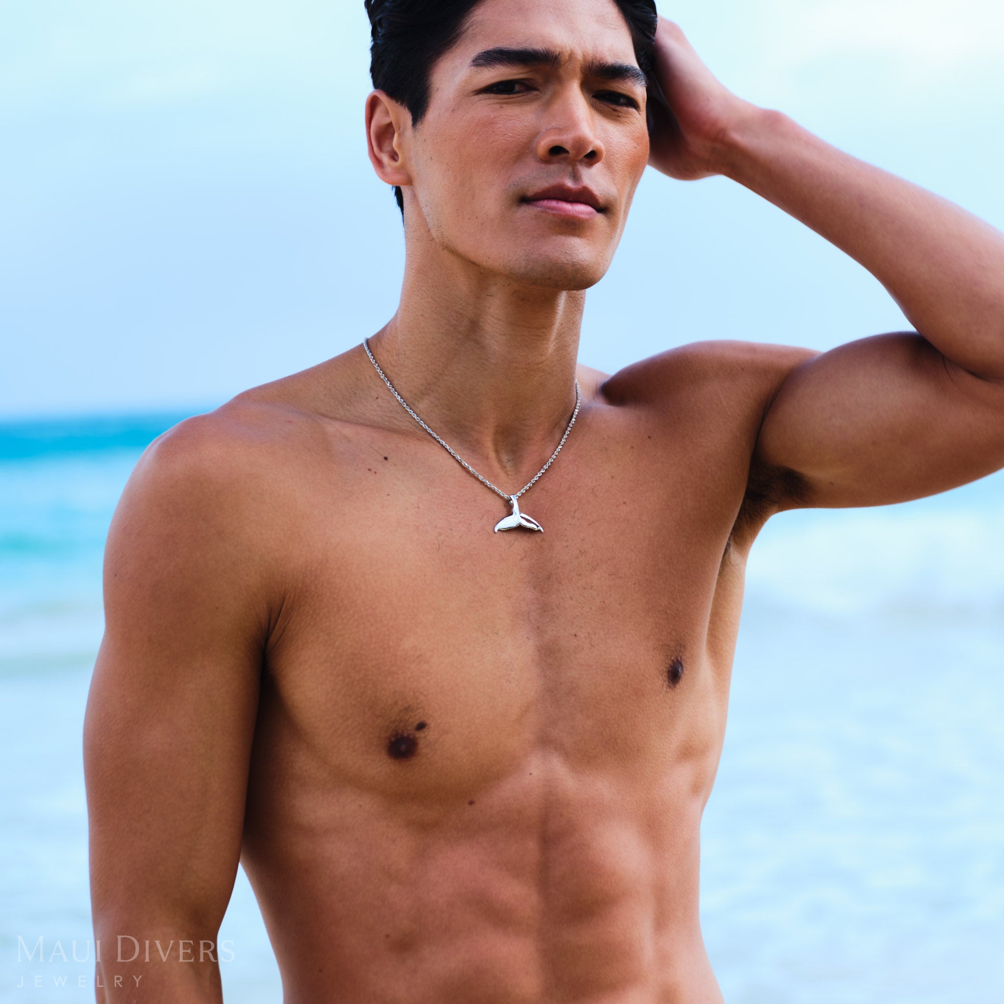 Man wearing a rope chain with a white gold whale tail pendant on a beach